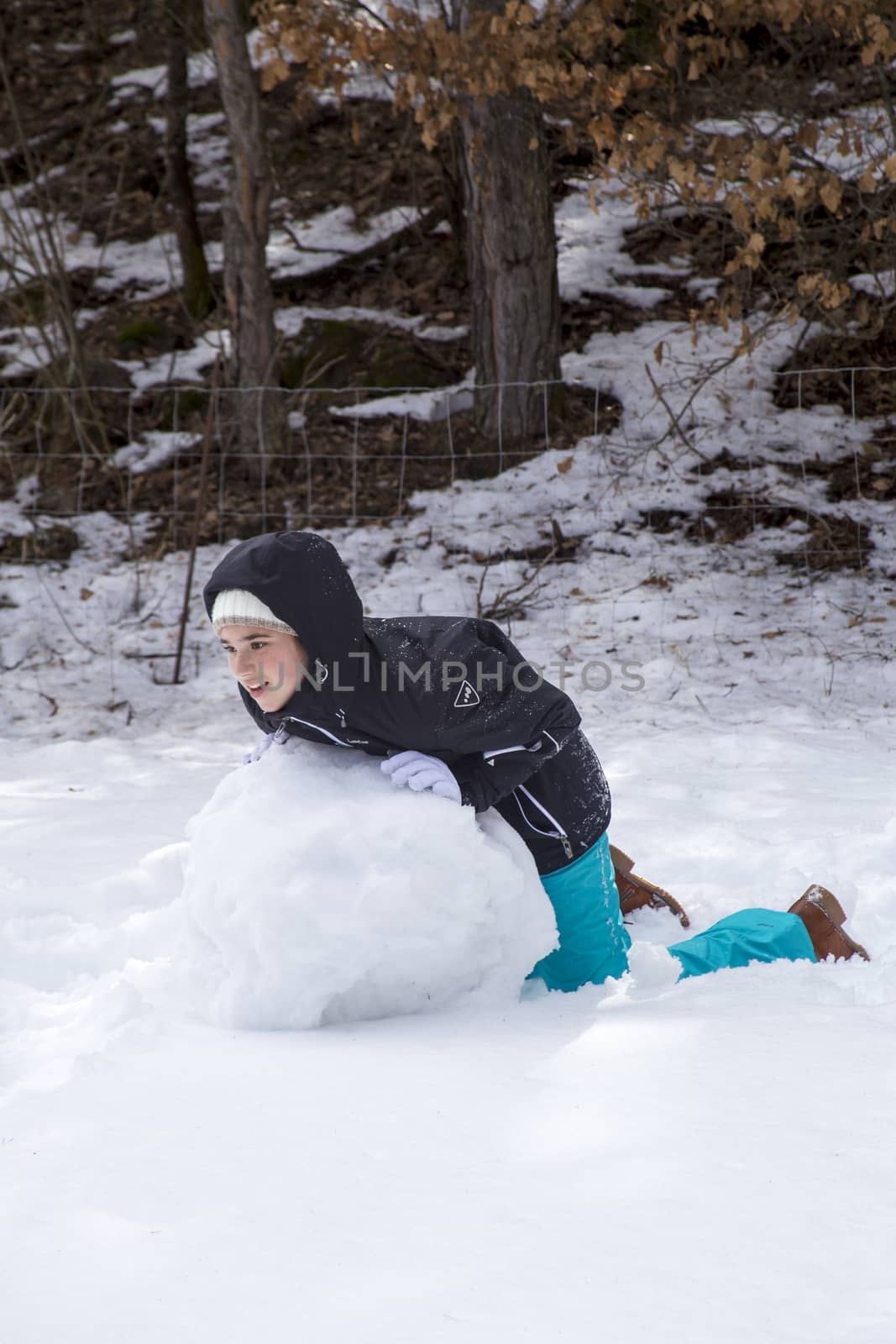 Young girl make a snowman on a sunny day in the winter snow-covered forest in the mountains.