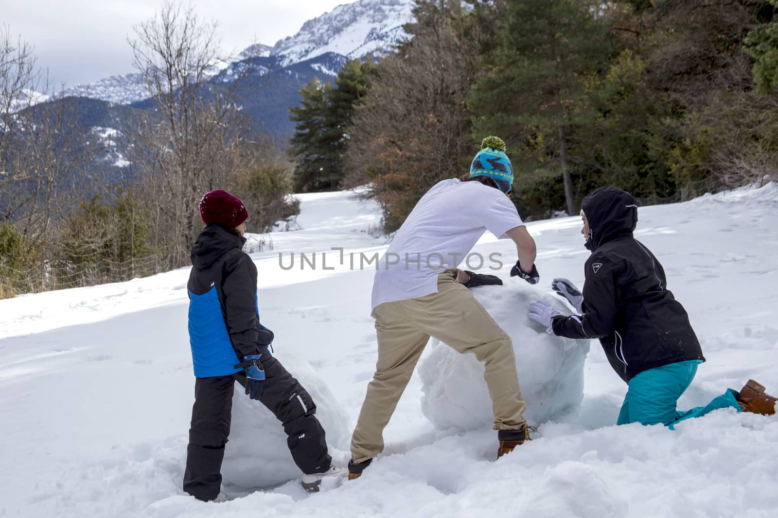 Young man, boy and girl make a snowman on a sunny day in the winter snow-covered forest in the mountains.