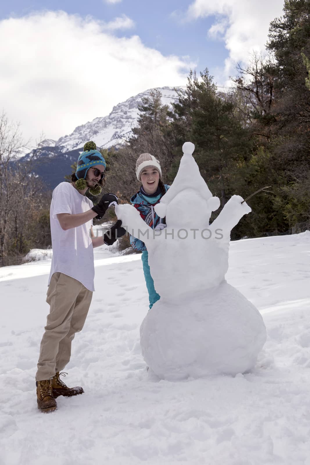 Young boy and girl make a snowman on a sunny day in the winter snow-covered forest in the mountains.