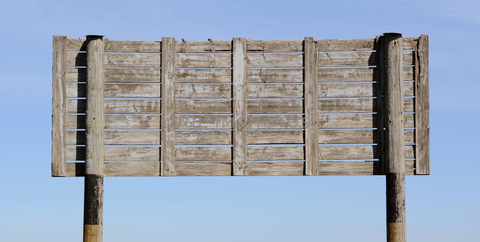 Weathered blank signboard of grey wooden planks against a blue sky