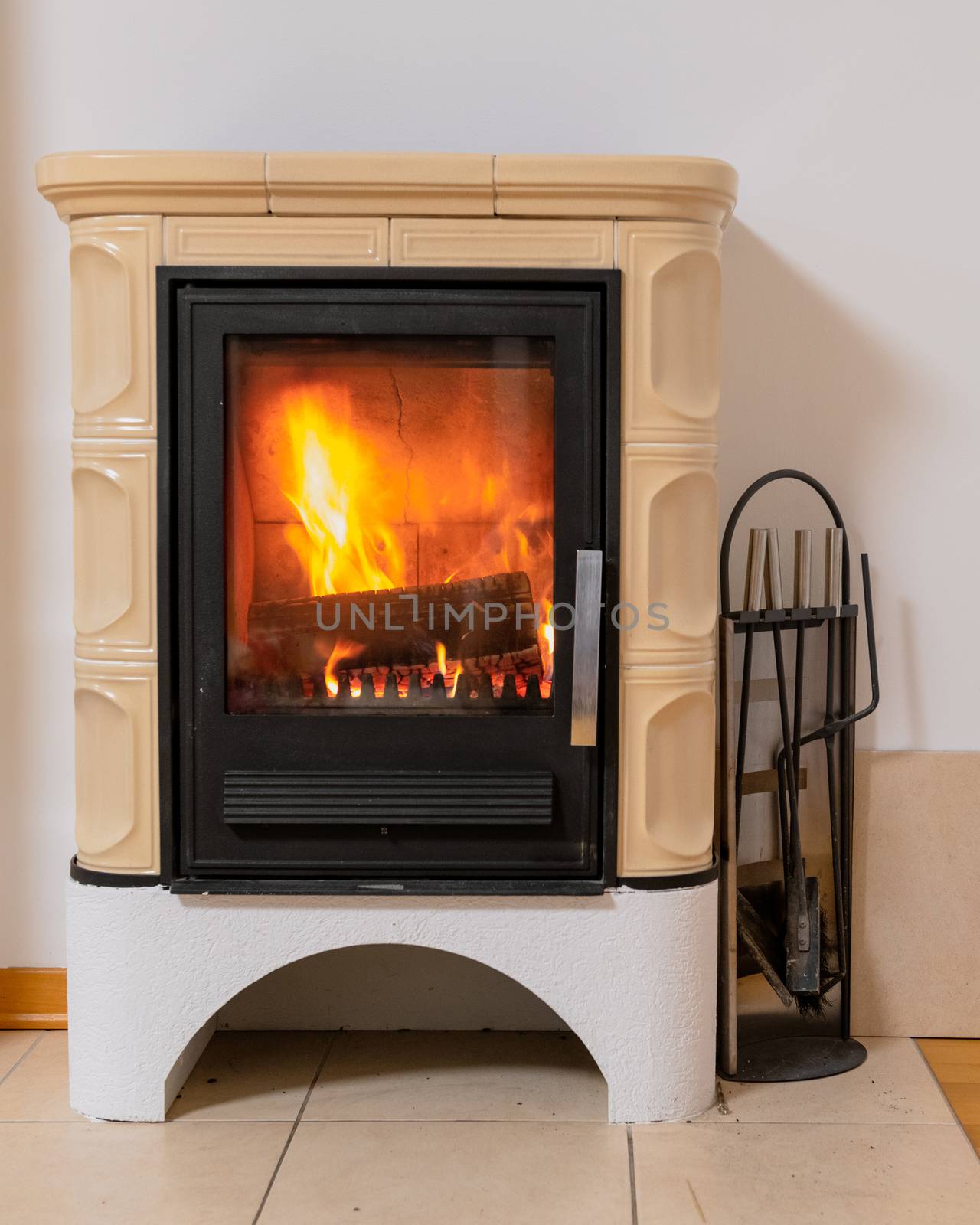 Tiled stove with fire burning inside, cosy and warm interior scene, heating in winter, Christmas decoration on the wall