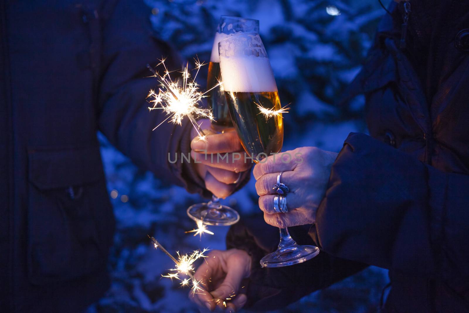 hands of elderly couple holding sparkles and glasses of champagne celebrating New Year