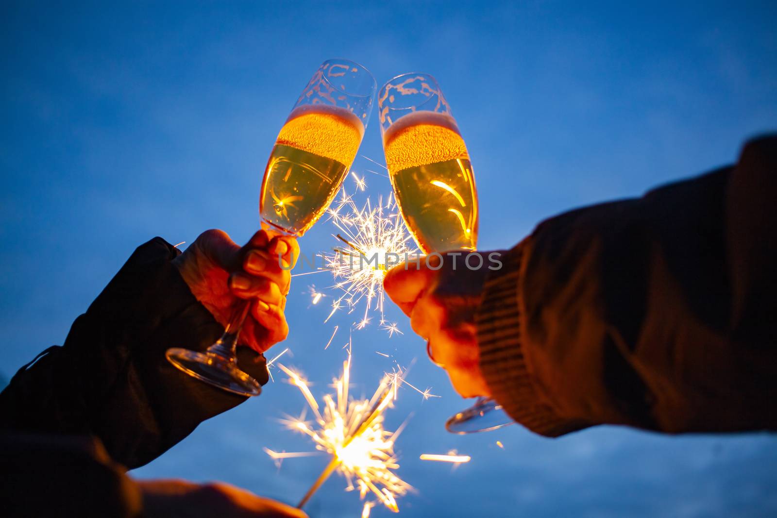 hands of elderly couple holding sparkles and glasses of champagne celebrating New Year