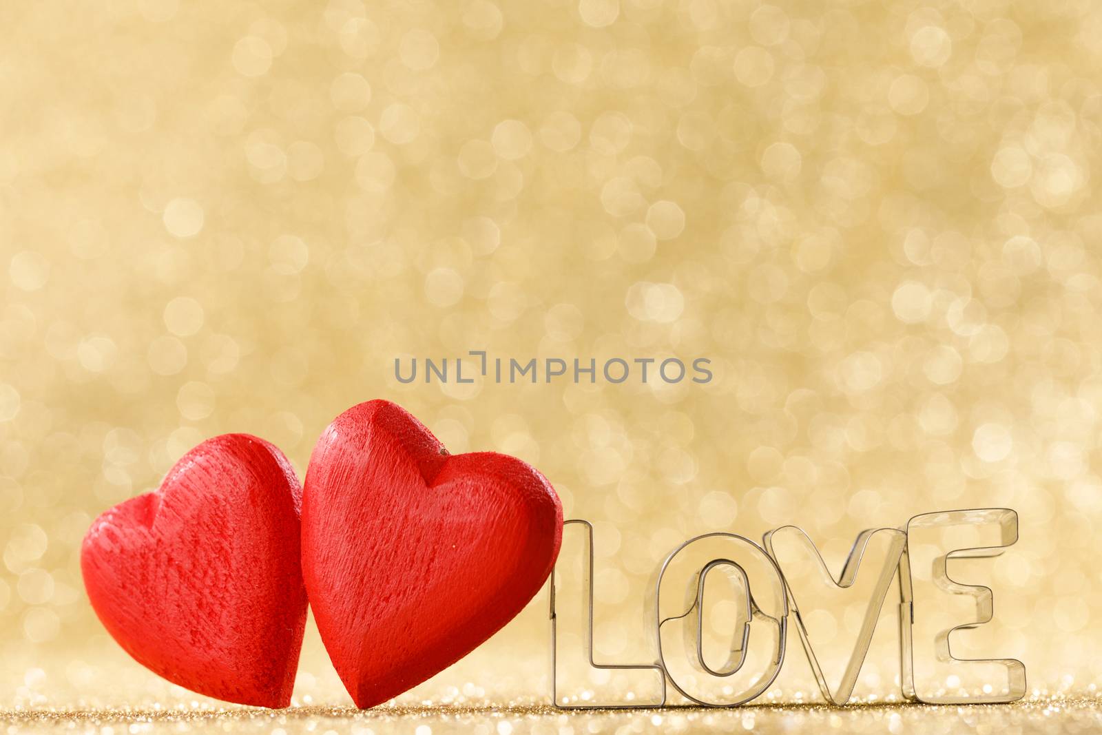 Two red handmade wooden hearts and word love on golden bright glitter lights bokeh background