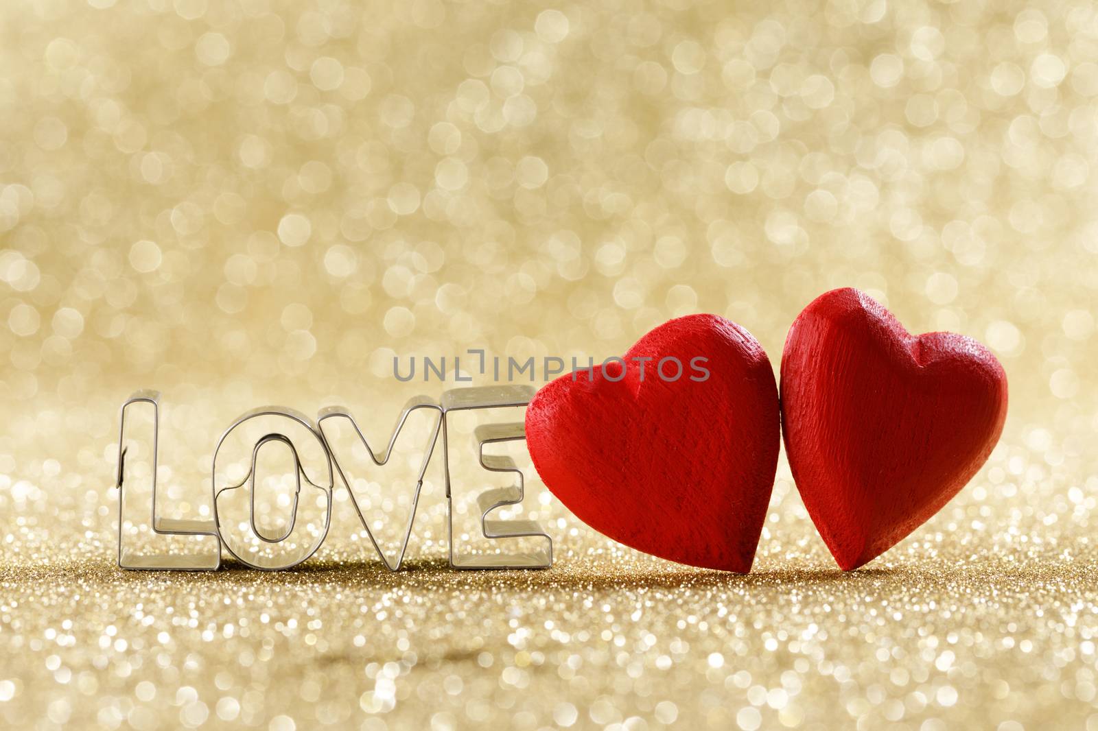 Two red handmade wooden hearts and word love on golden bright glitter lights bokeh background