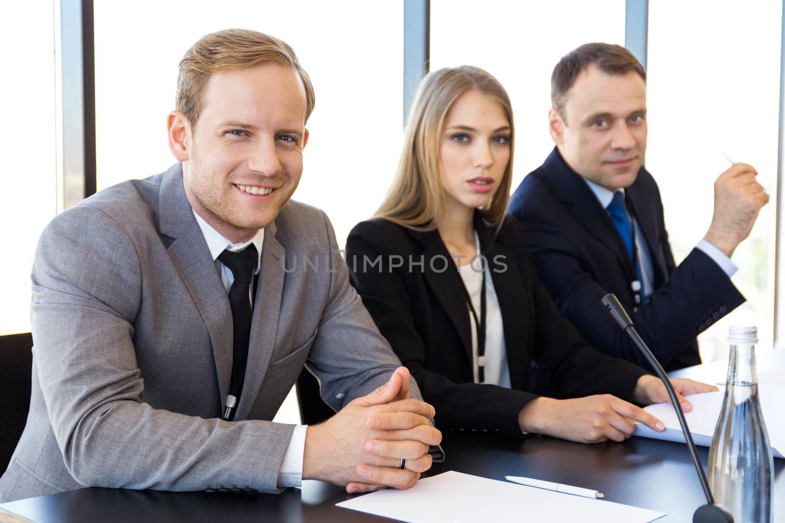 Close-up of participants of press conference sitting at the table in a row in front of audience