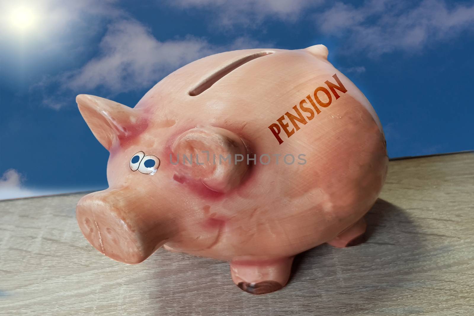 Piggy bank, good luck pig with lettering Pension on wooden surface in front of blue sky background