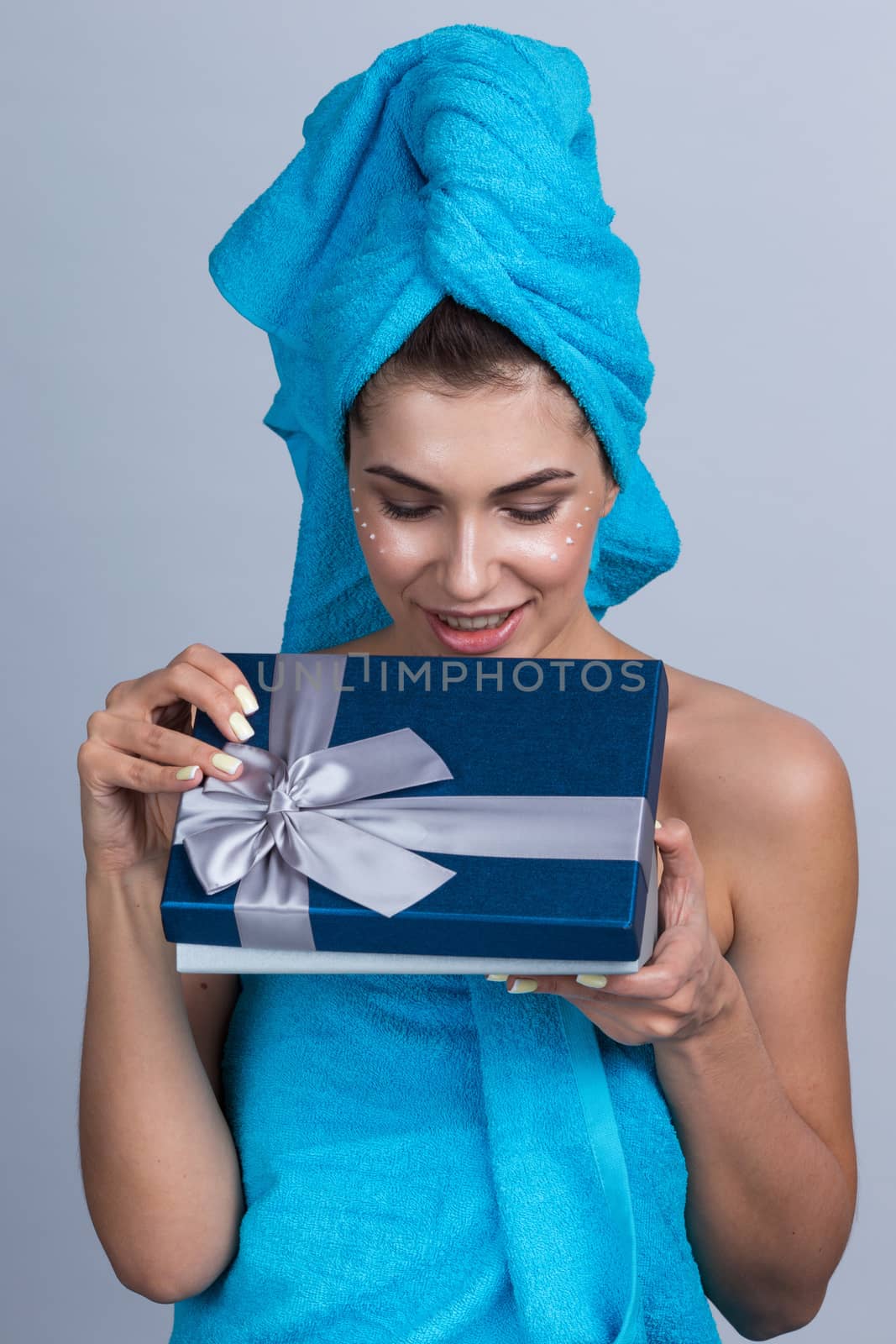 Beautiful young woman after shower with towel on head and creme on her face open beauty holiday gift