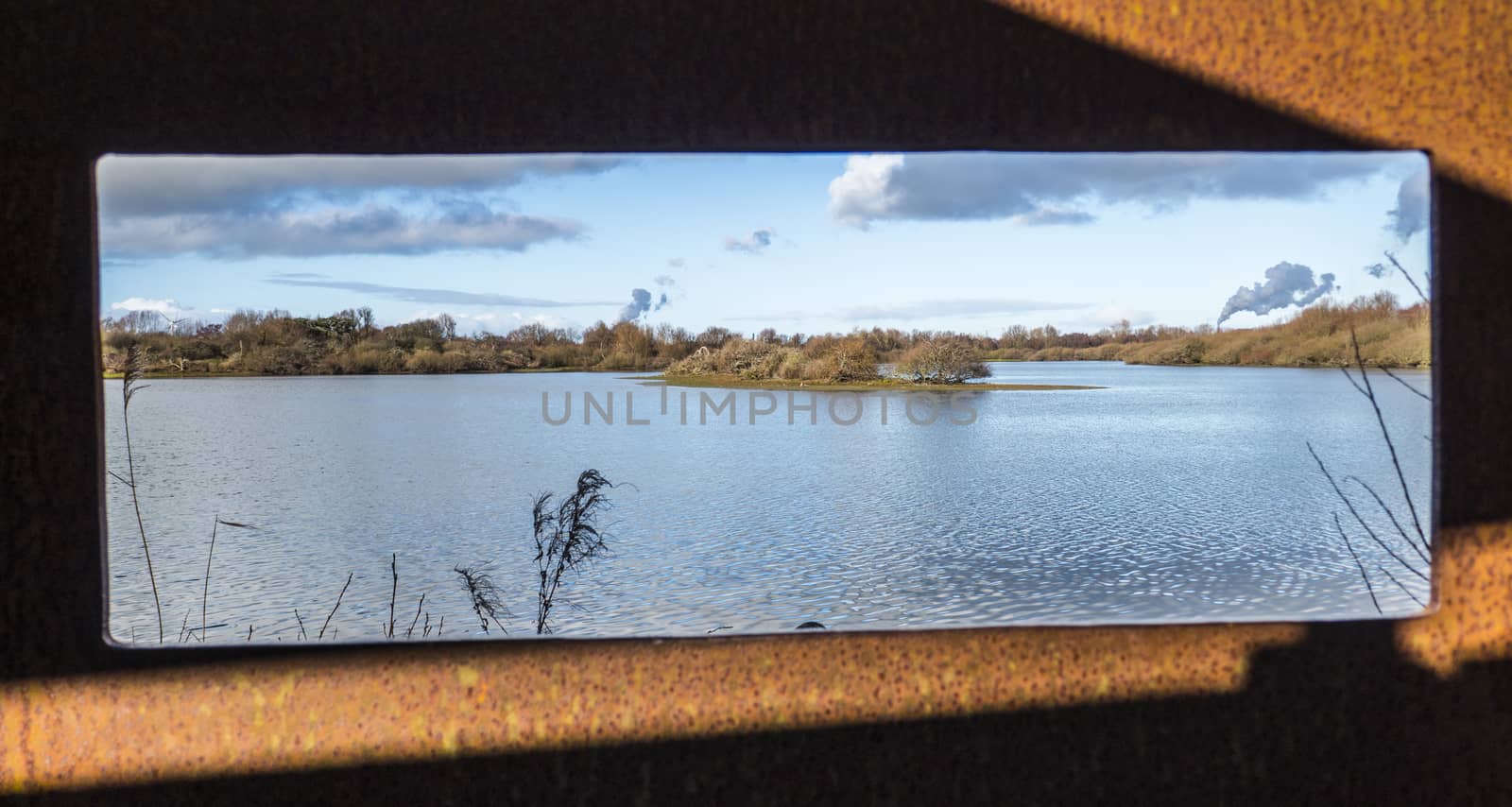 view from a viewpoint at water in Holland with a pond, water plants small islands and the smoke from the europoort industry at the background