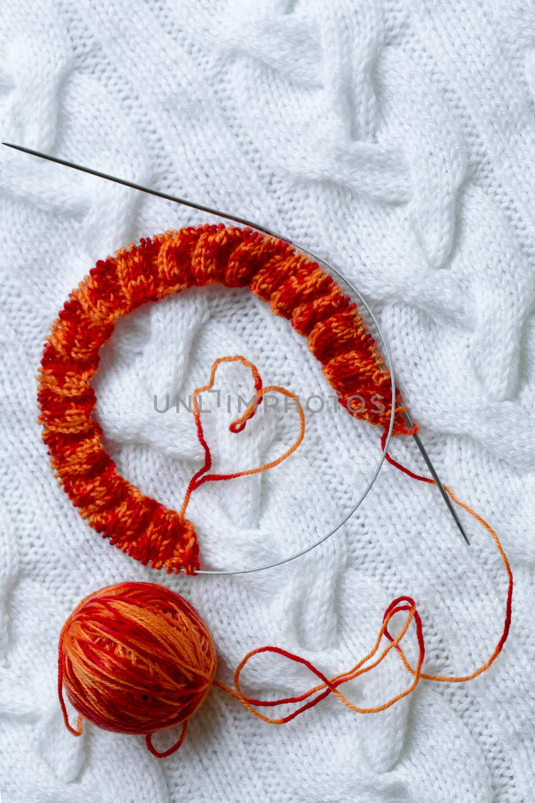 Knitting project in progress. A piece of knitting with a ball of yarn, knitting needles and a heart lined with thread.