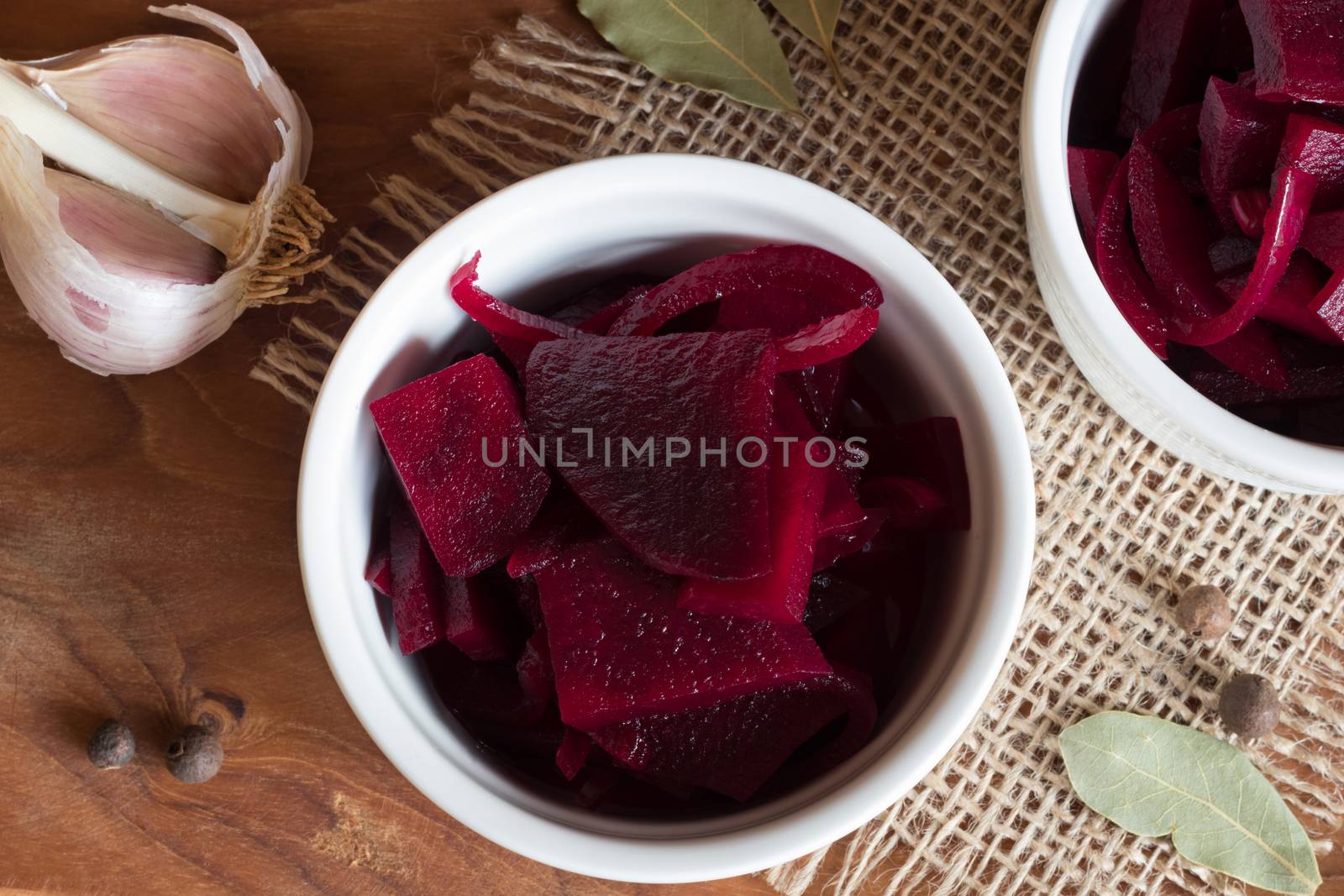 Fermented red beet in a bowl, with garlic, bay leaf and allspice in the background, top view