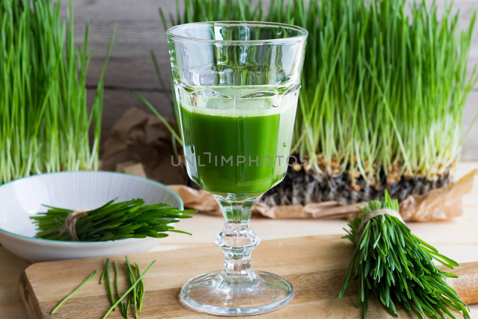 A glass of wheatgrass juice with freshly harvested wheatgrass on a wooden table