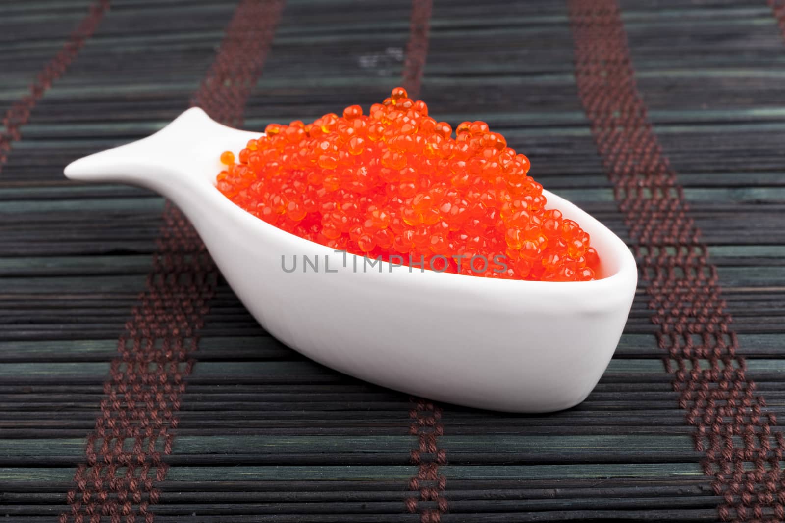 Red caviar in a fish shape bowl on dark wooden background