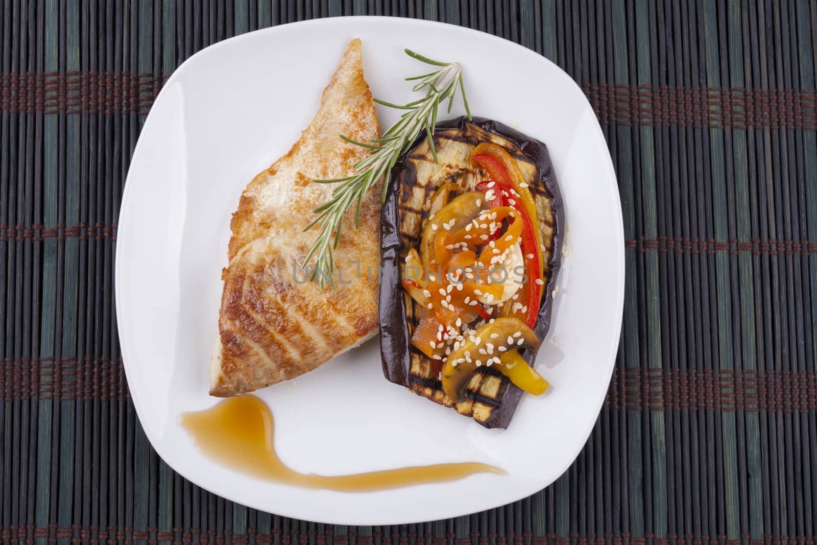 Fish and vegetables on eggplant in white plate on dark background