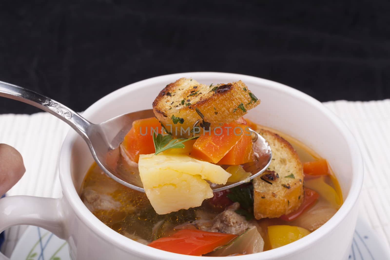 Vegetable soup on a spoon with bread close-up  on dark background