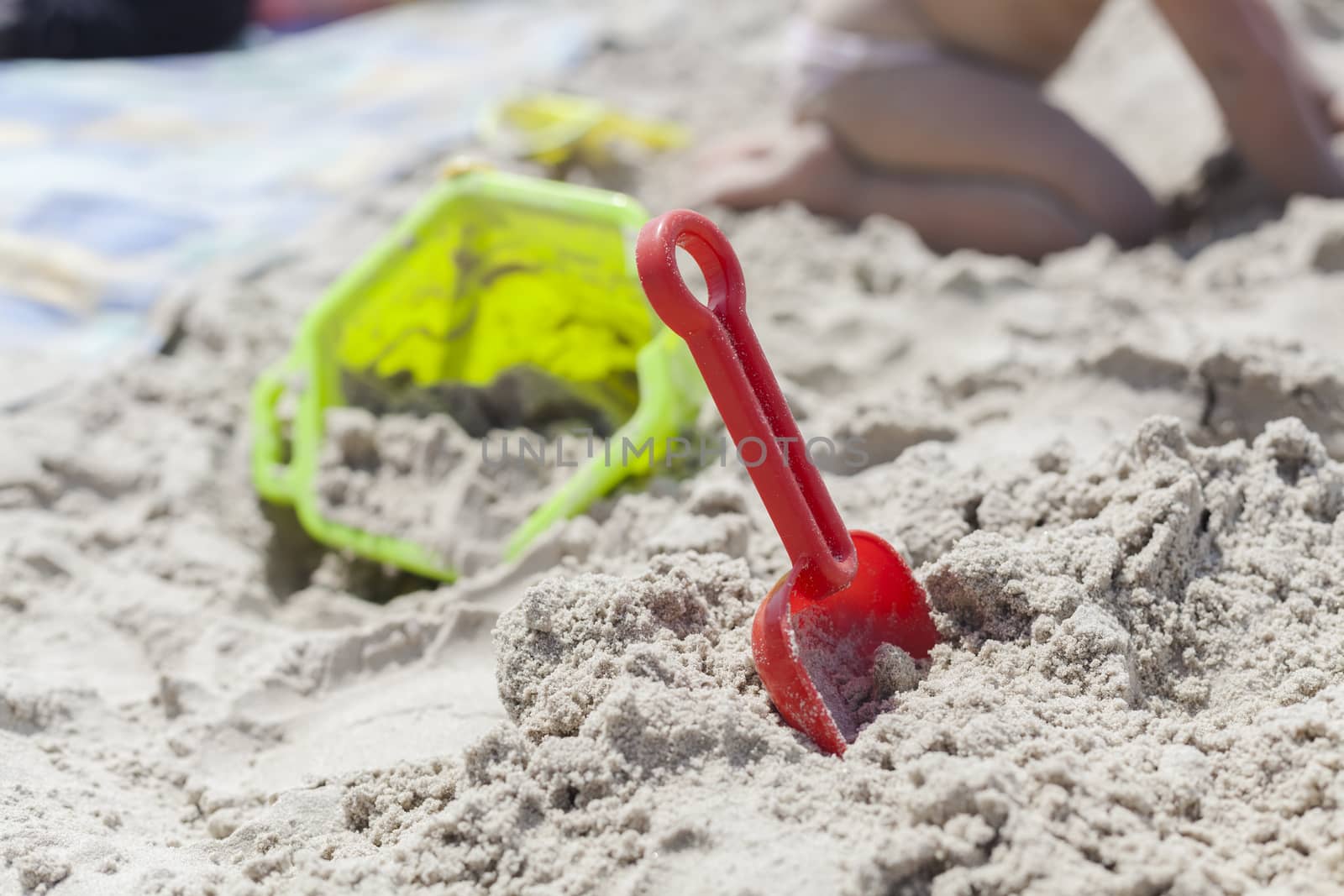 Red toy shovel in the sand with a green bucket in the background