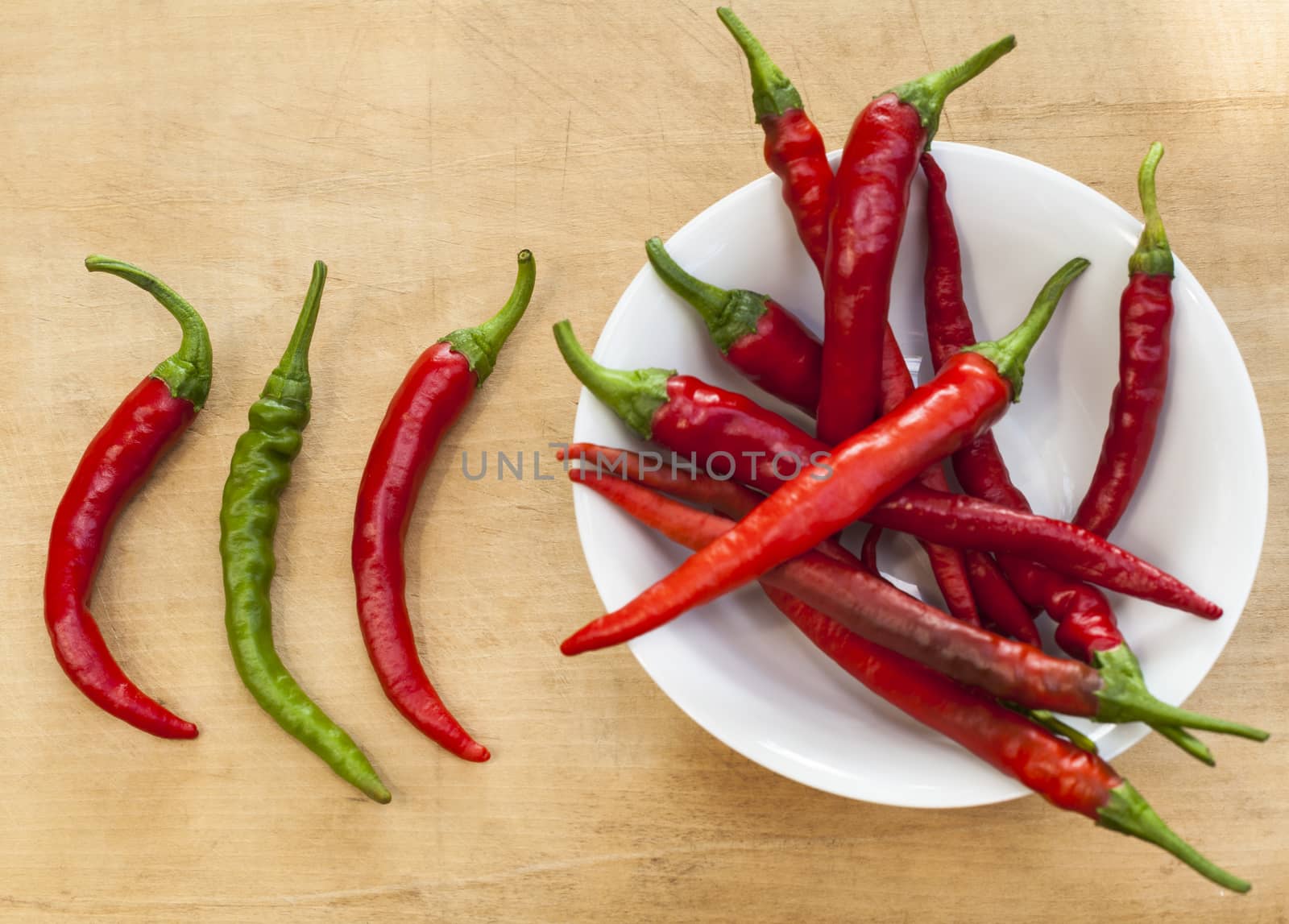 2 chili red peppers and a green one beside a bowl full with red chilis 