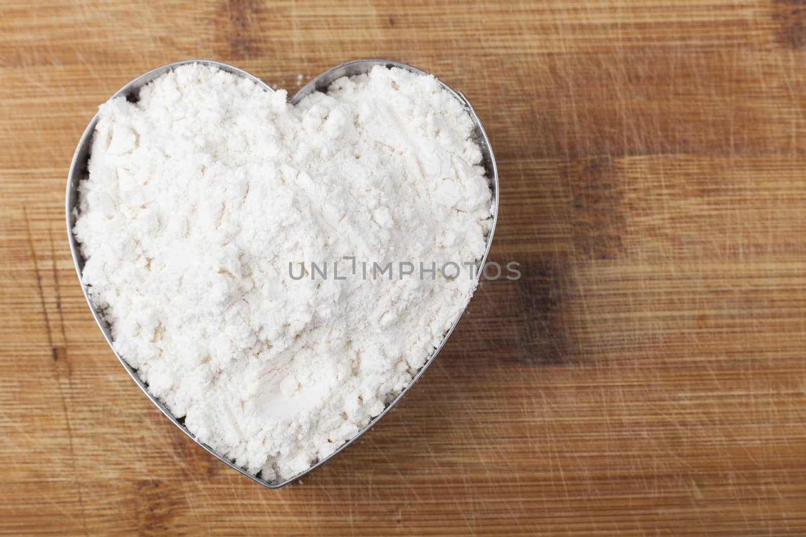 Flour shape heart in a mold on brown wood cutting board