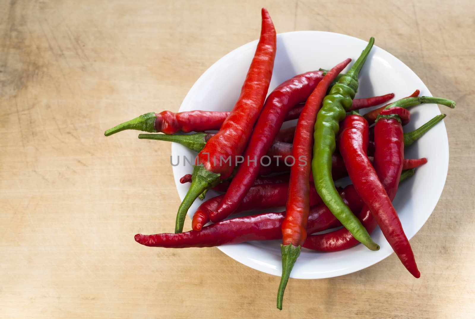 Red chili with one green cilli pepper in a bowl on wood background