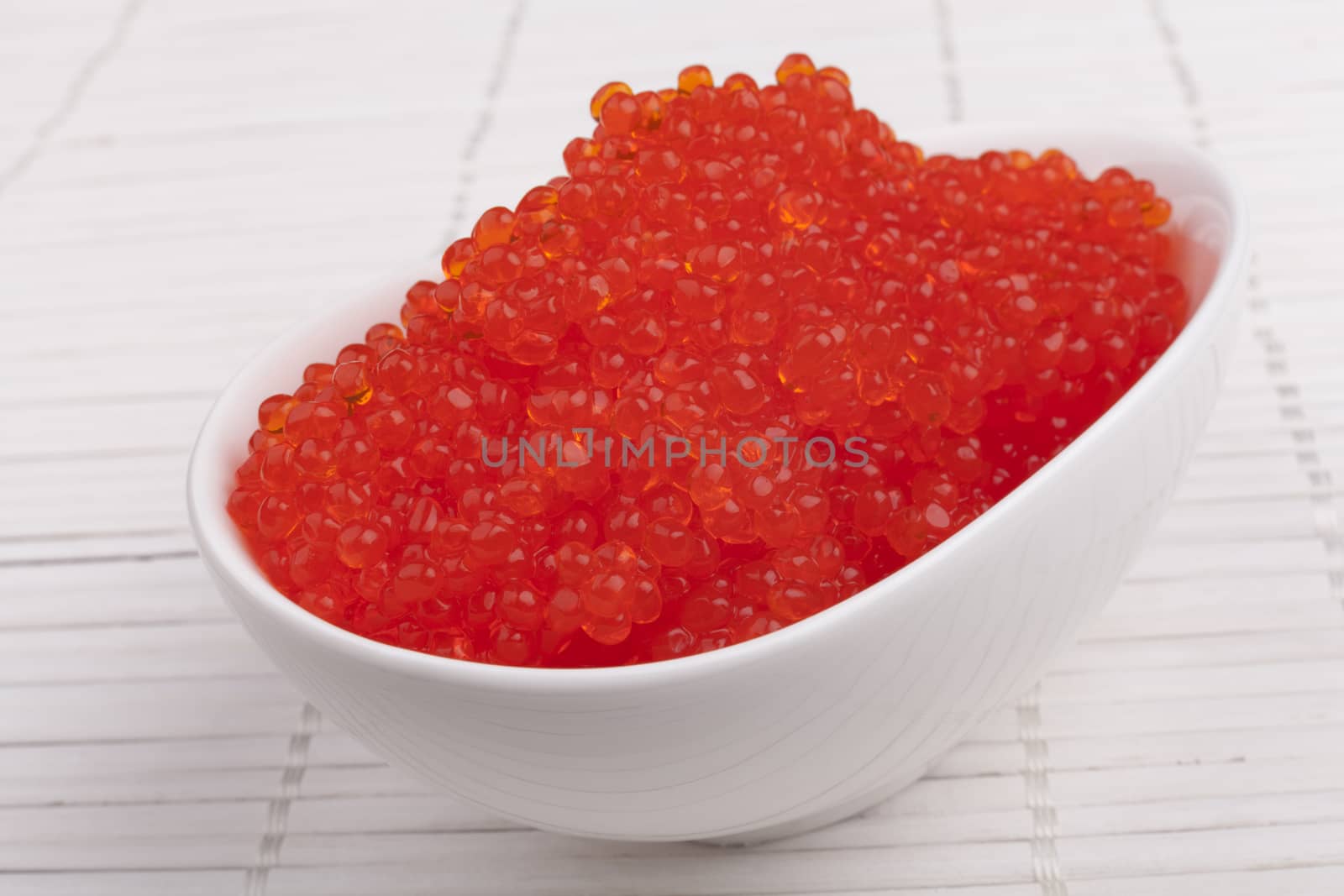 Red caviar in a white bowl on white wooden background
