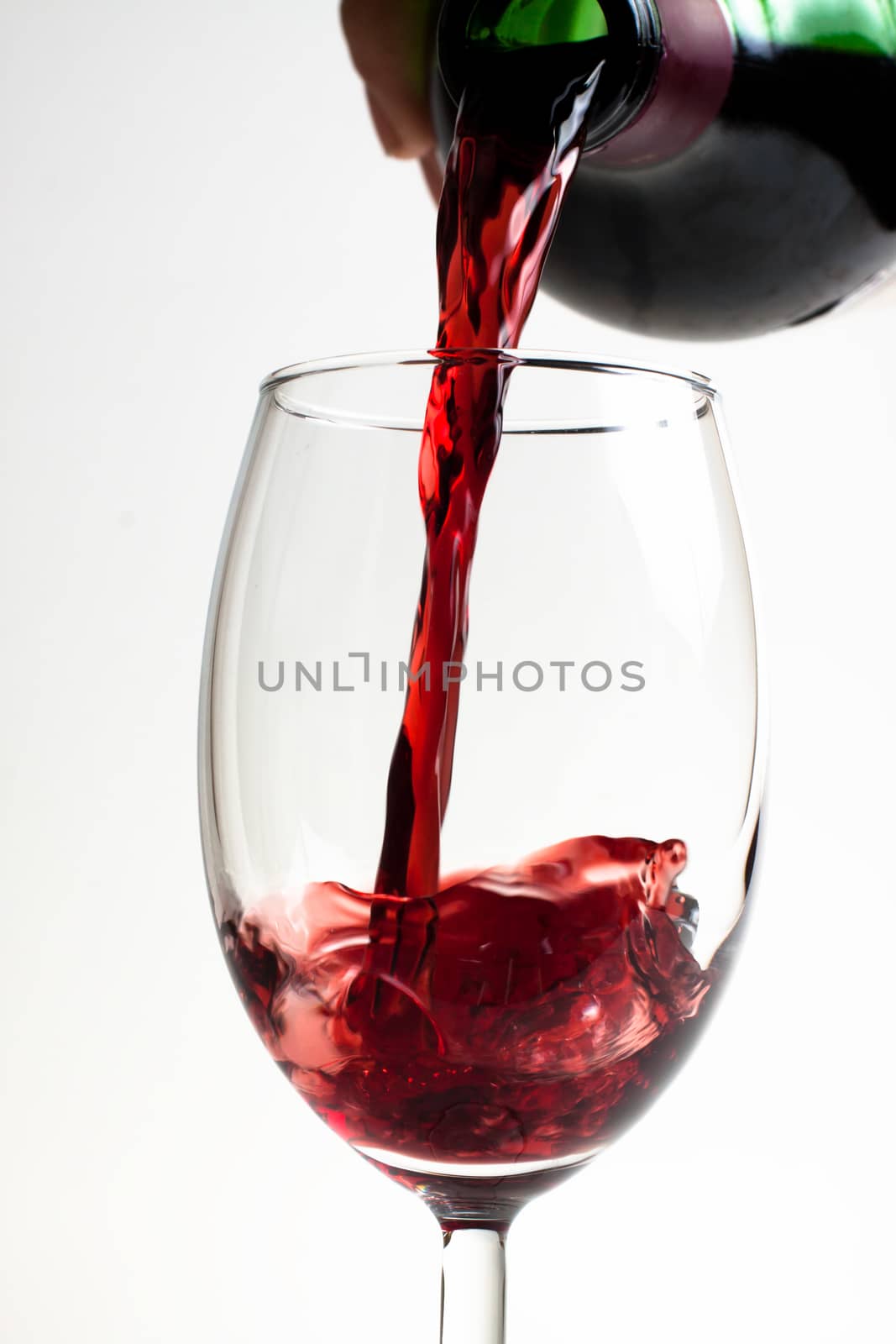 red wine puring from bottle to glass close-up on white background