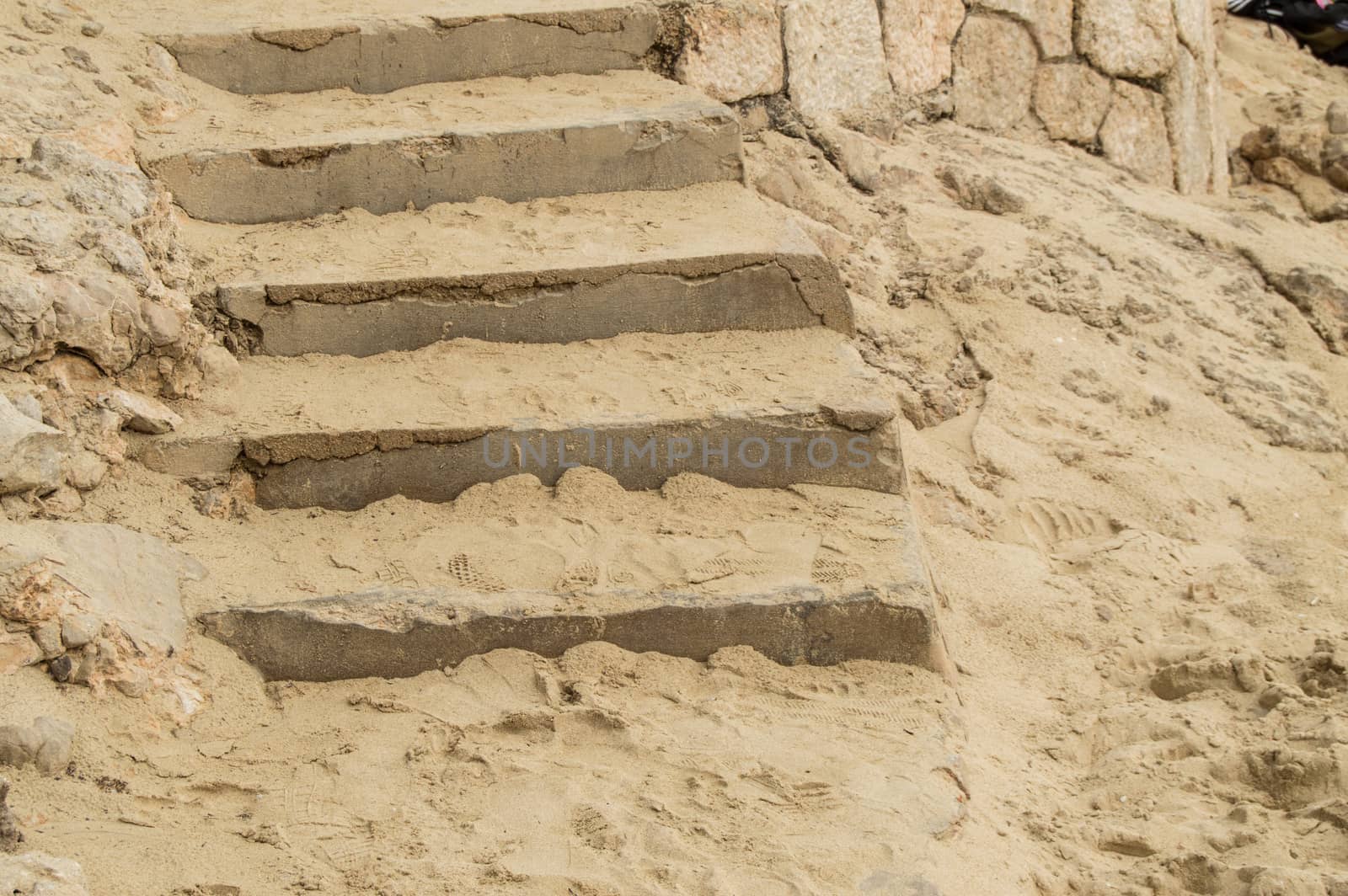 Close-up of stone stairs and sand on the Mediterranean beach, background footprints in the sand.