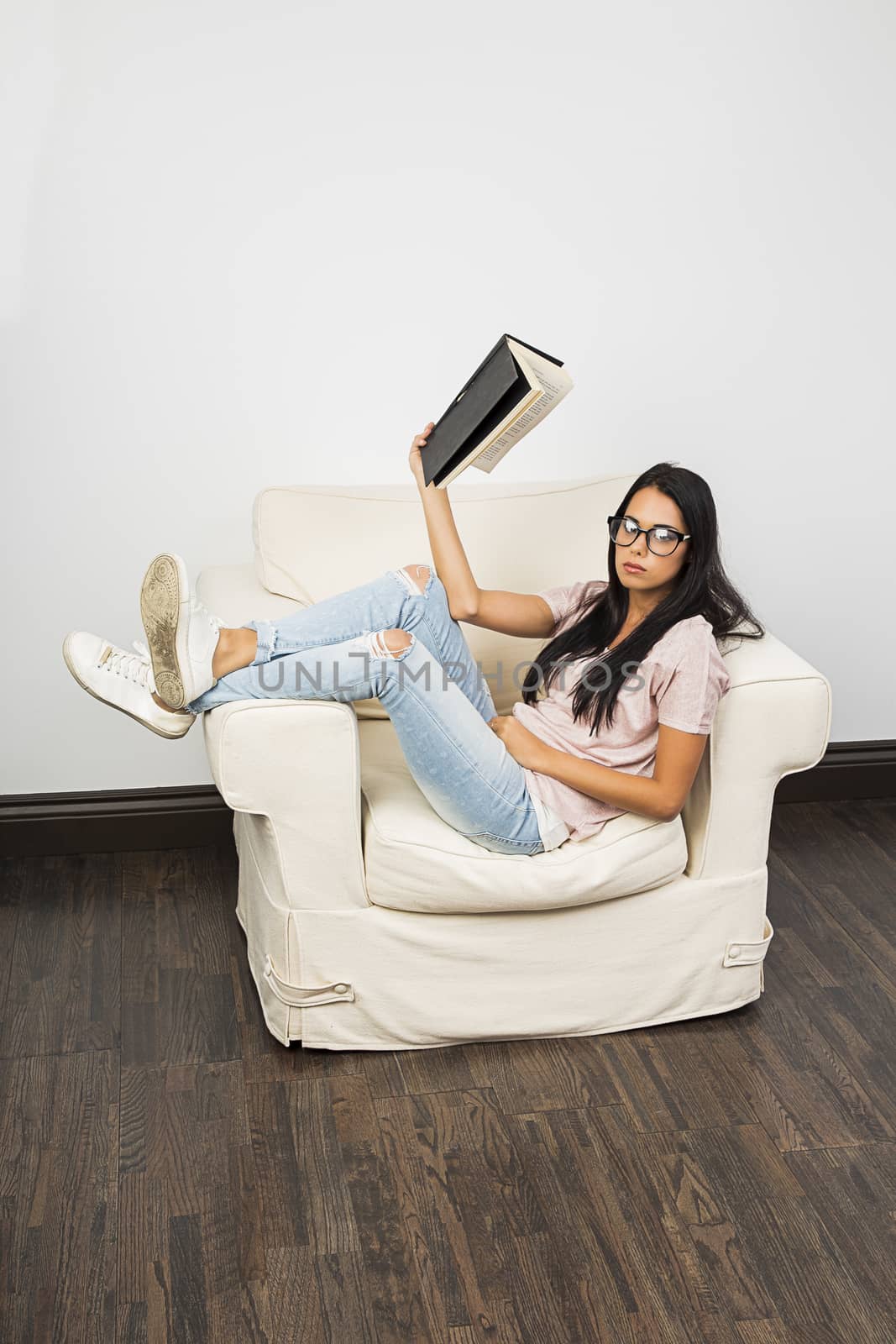 twenty something sitting on a couch with leg up, reading a book

