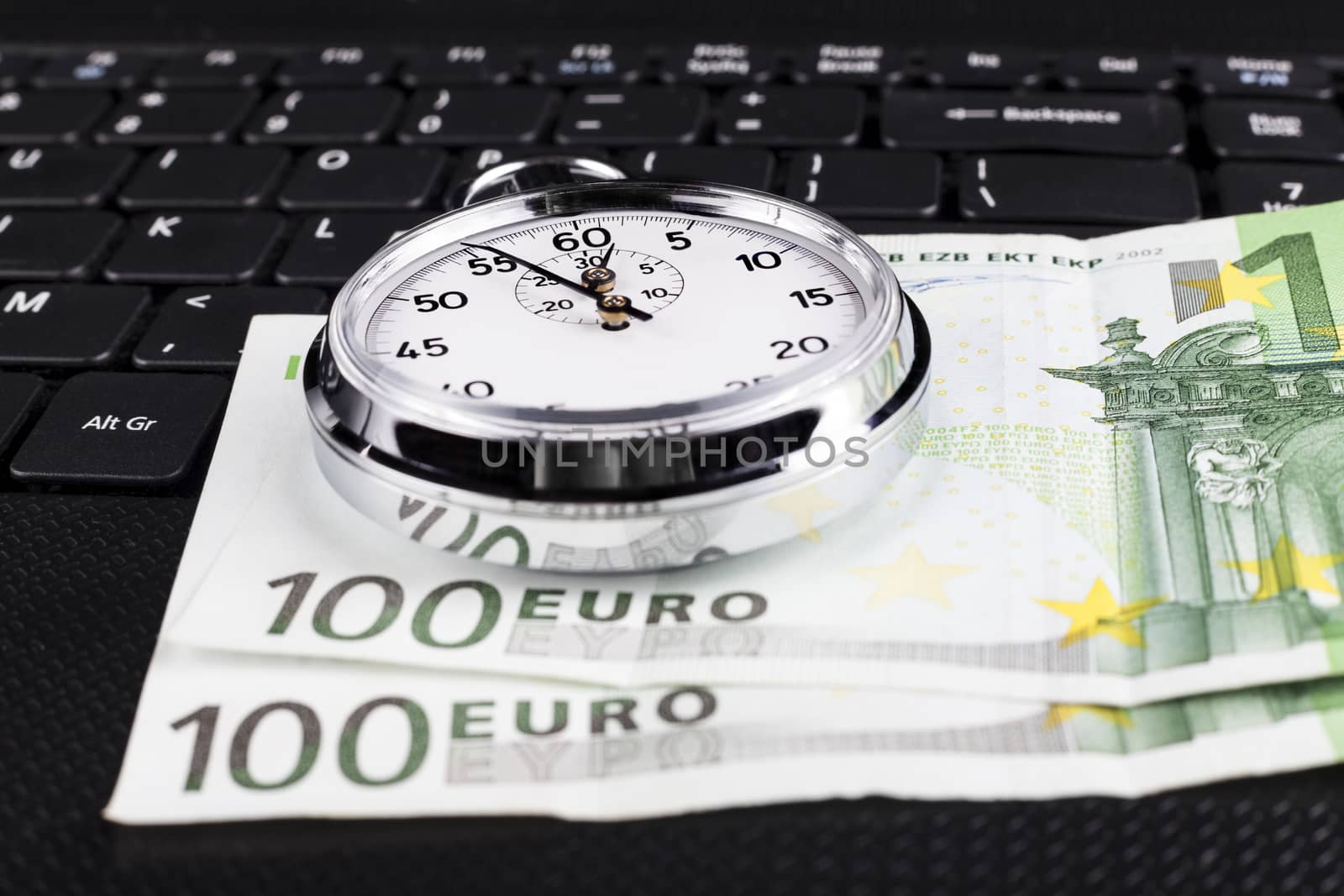 Silver stopwatch on black laptop keyboard with 100 euro bills