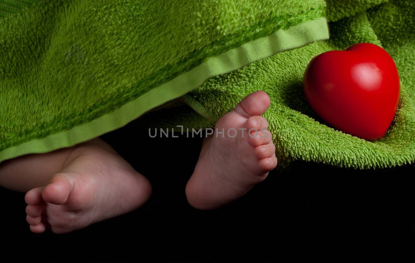 baby feet and a red heart covered with green towel on balck background