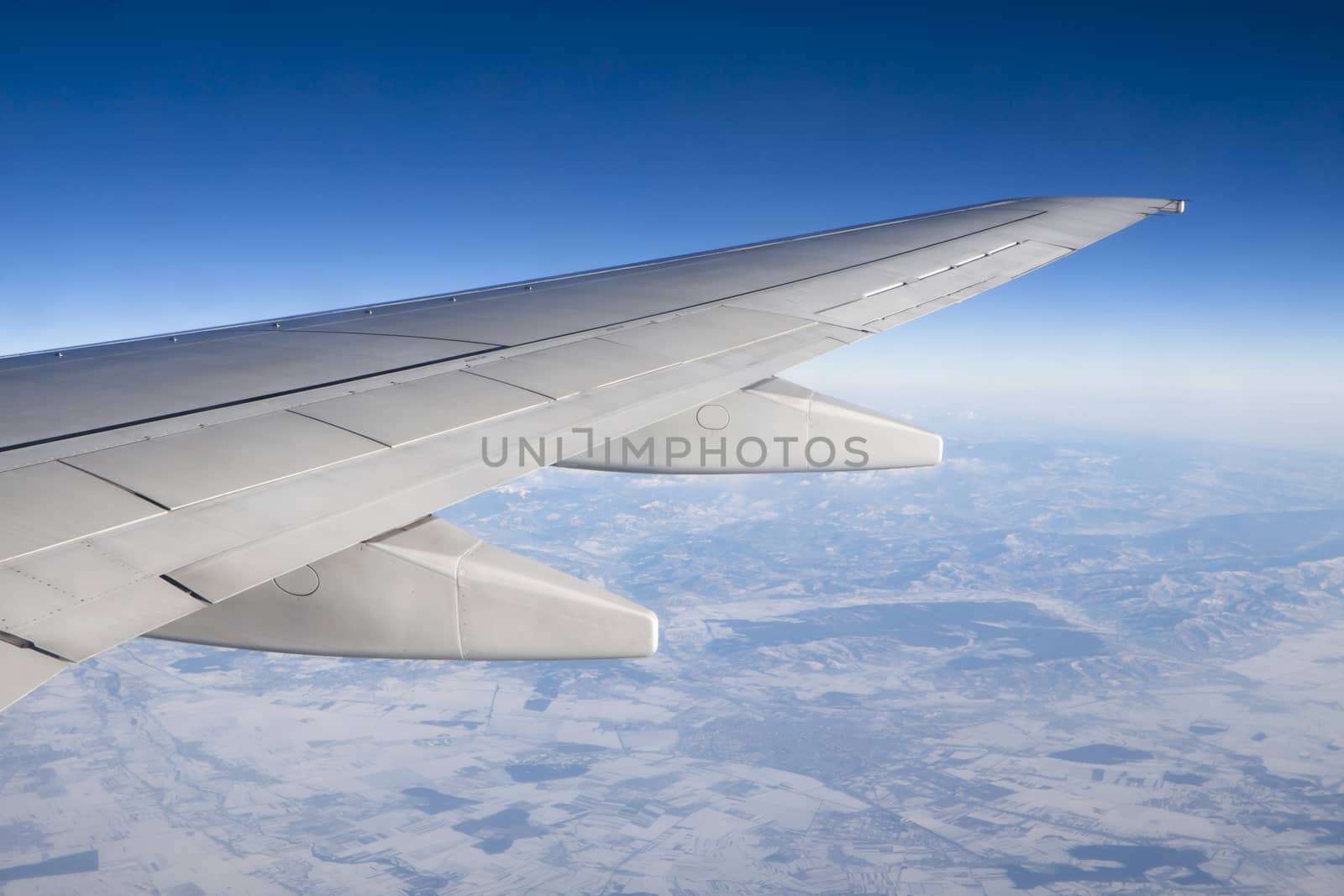 airplane wing in the air trough the window with terestrial view and blue sky