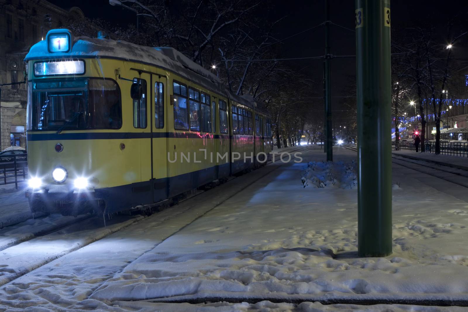 yellow tram in a cold winter night with snow and ice on it