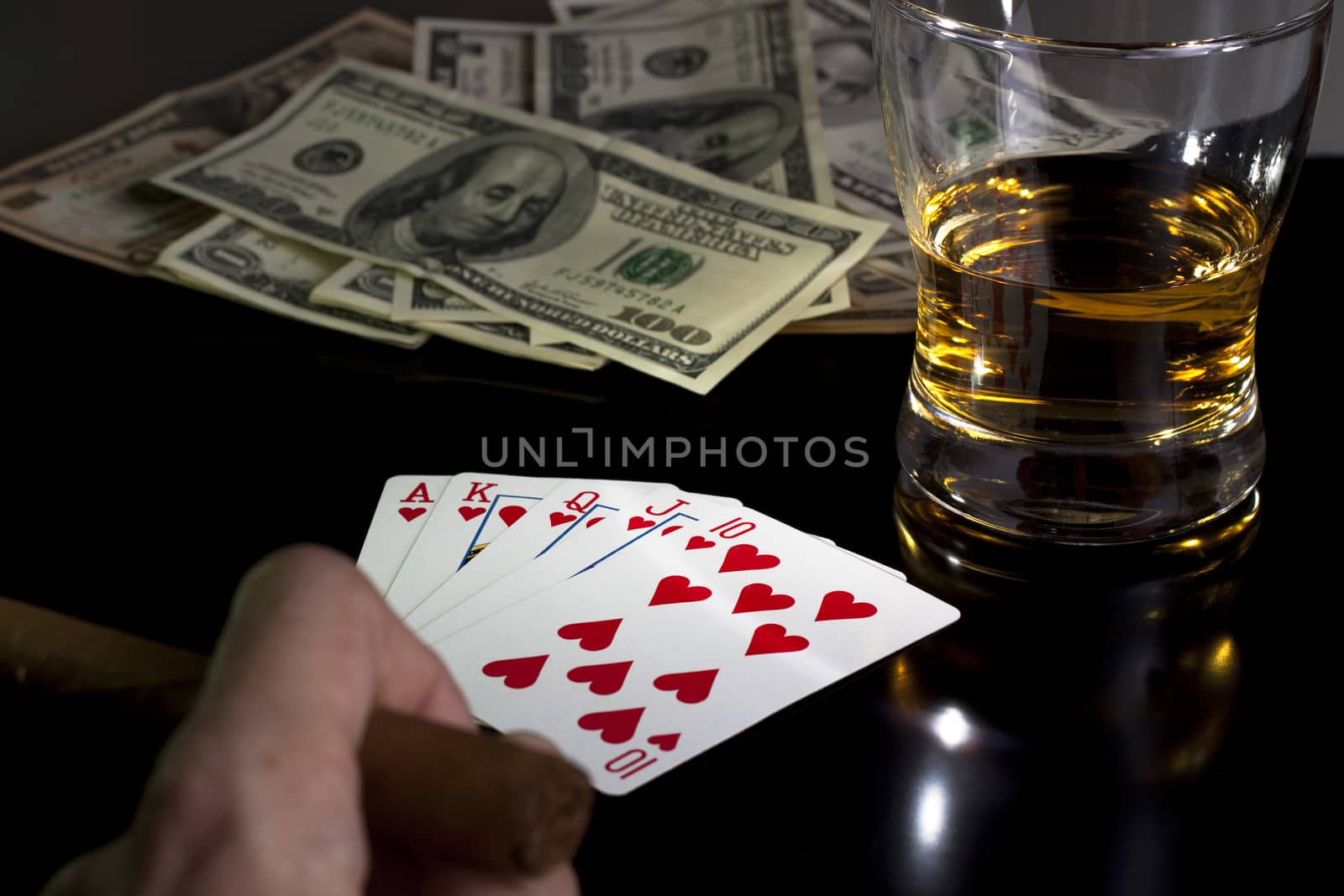 poker playing cards whiskey and some money on a table with reflection