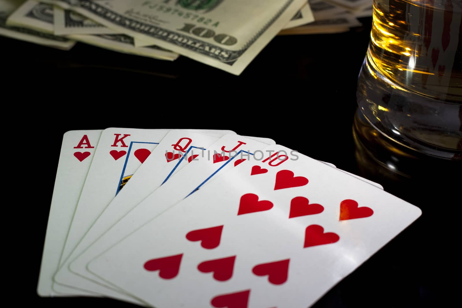 poker playing cards whiskey and some money on a table with reflection