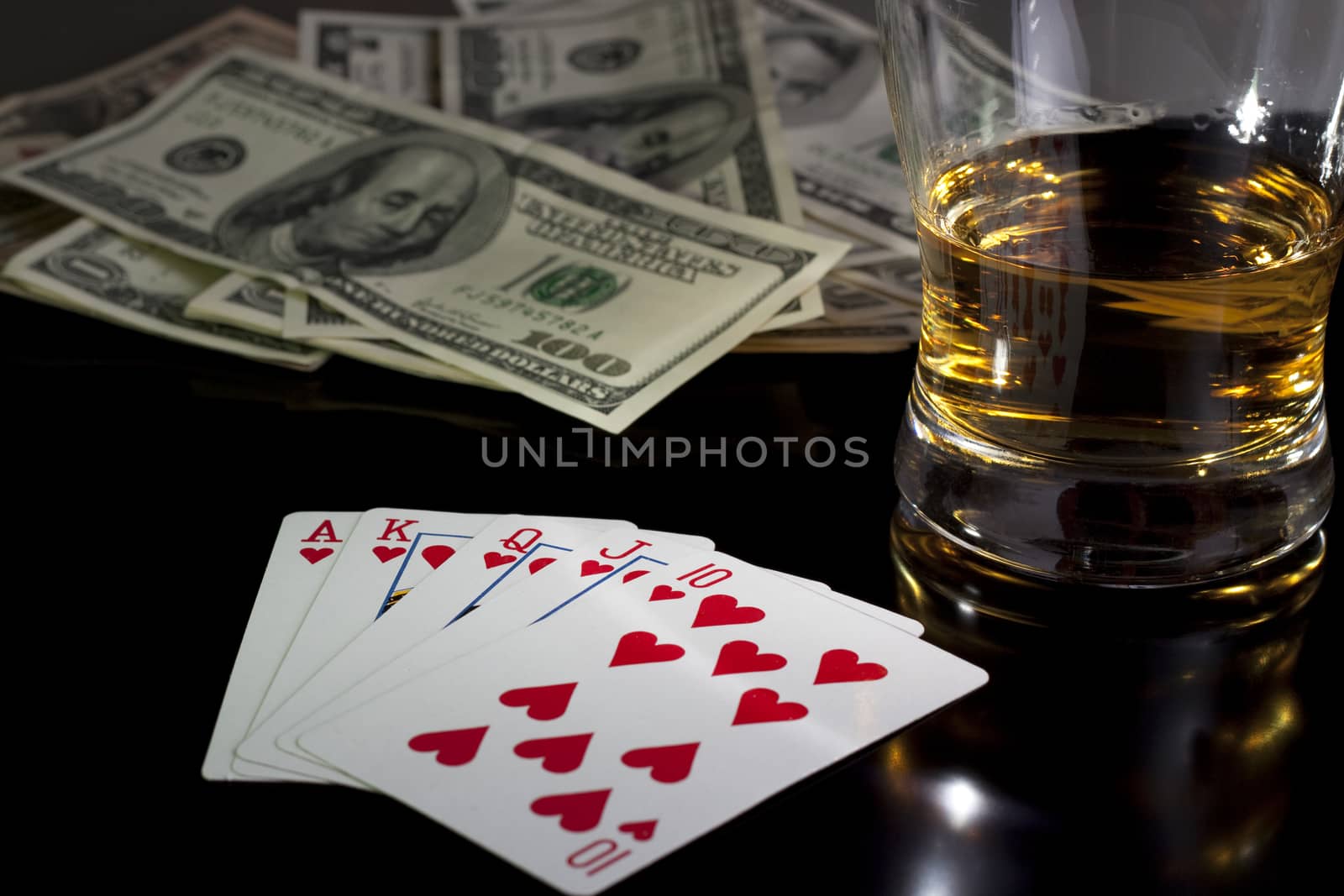 poker playing cards whiskey and some money on a table with reflection