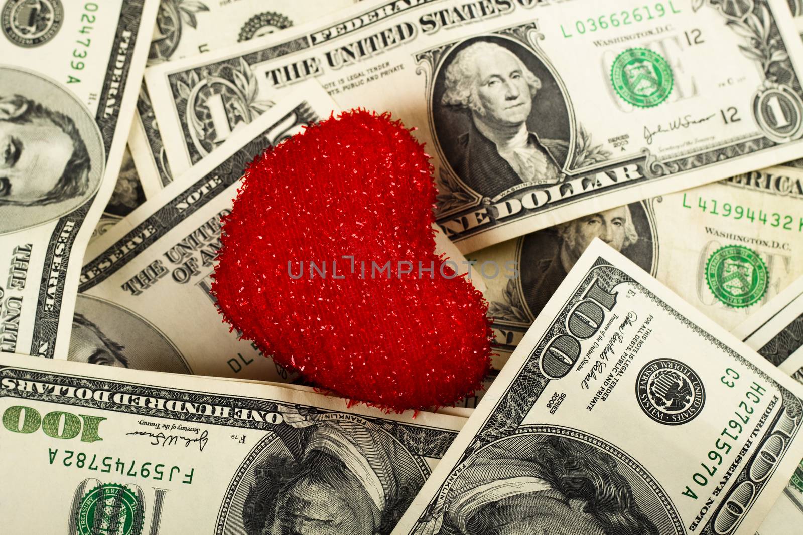 a small red heart on a pile of dollar dills