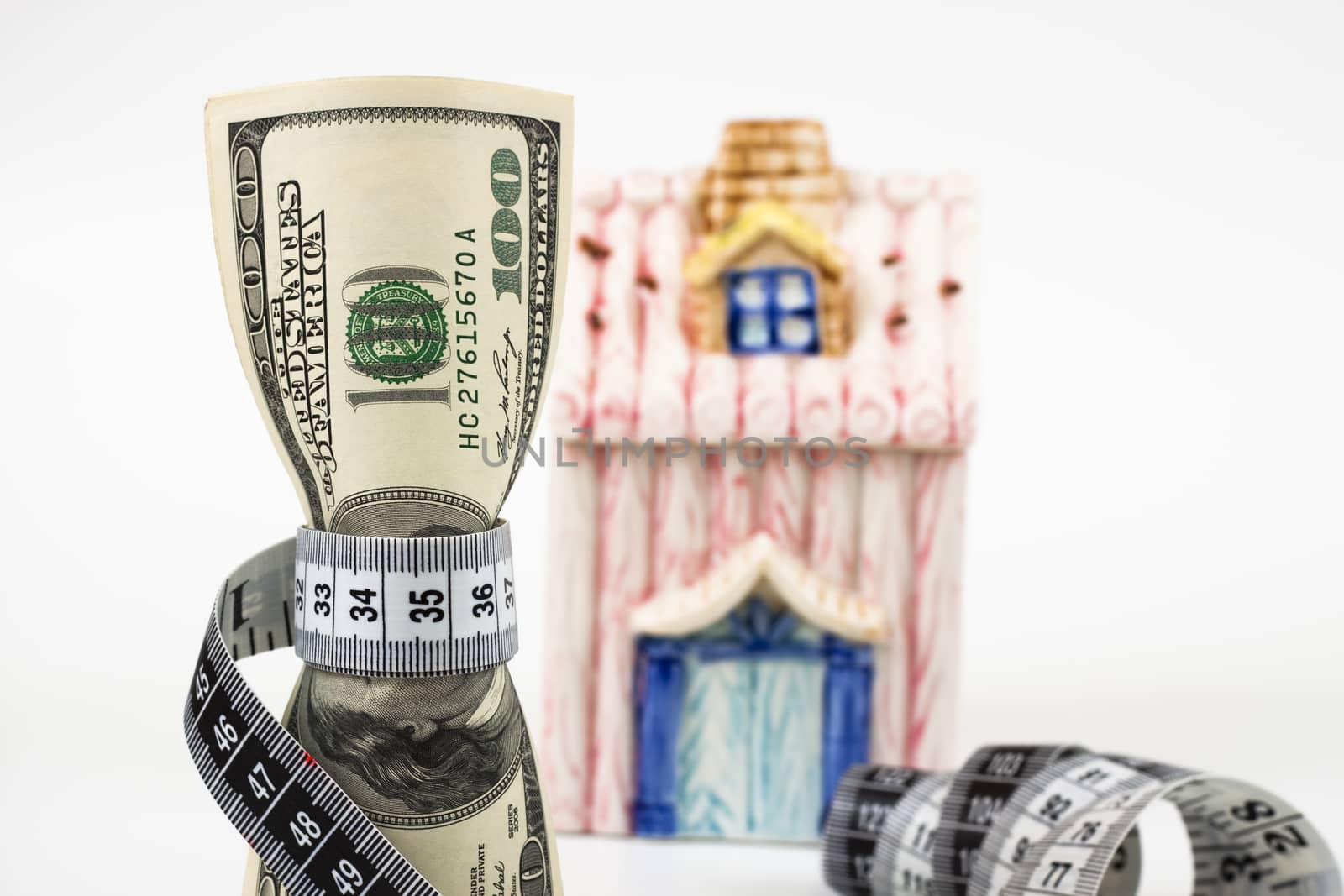 100 dollar bills tight with a measuring tape a small house in the background white background