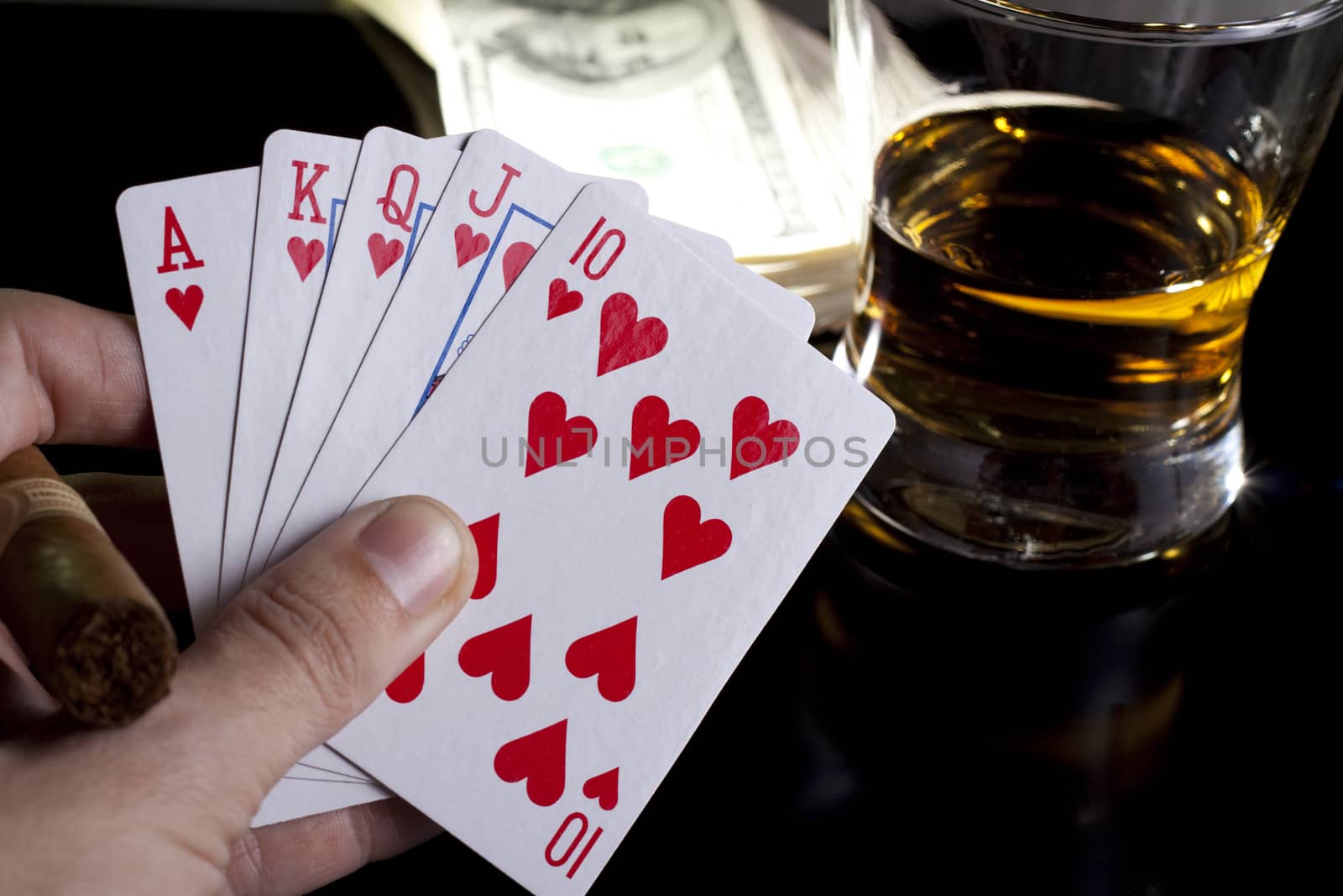 poker playing cards whiskey and some money on a table with reflection