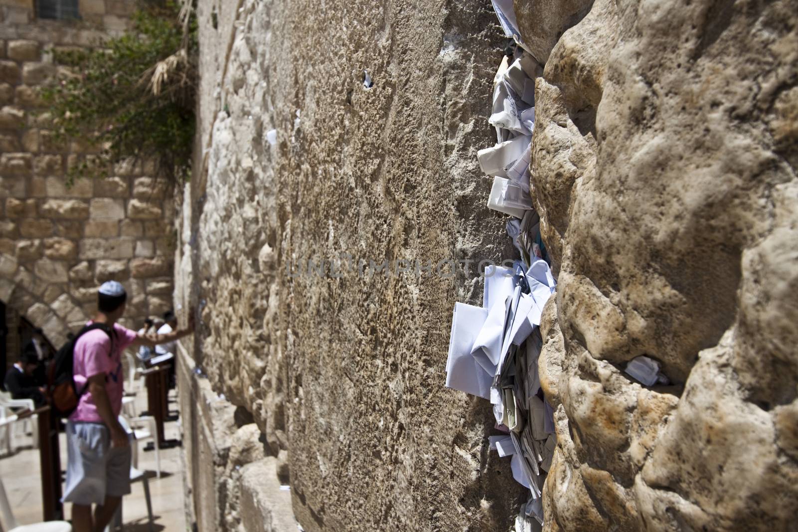 notes in the western wall and a man holding his hand on the wall while praying