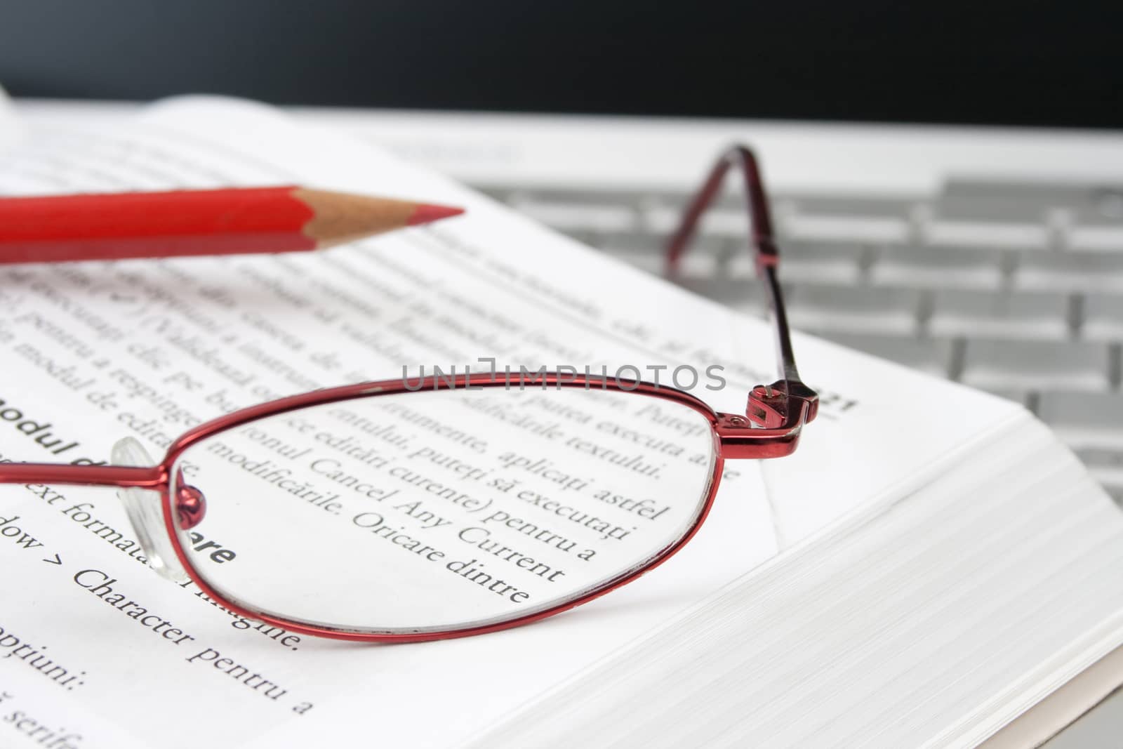open book on a laptop with a pair of red glasses and a red pencil