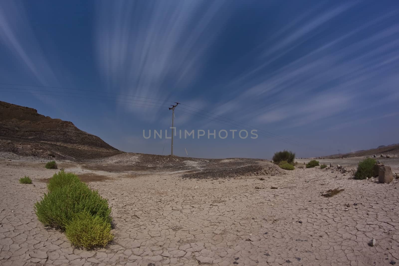 elecricity pole in the desert with blue cloudy sky and cracked land