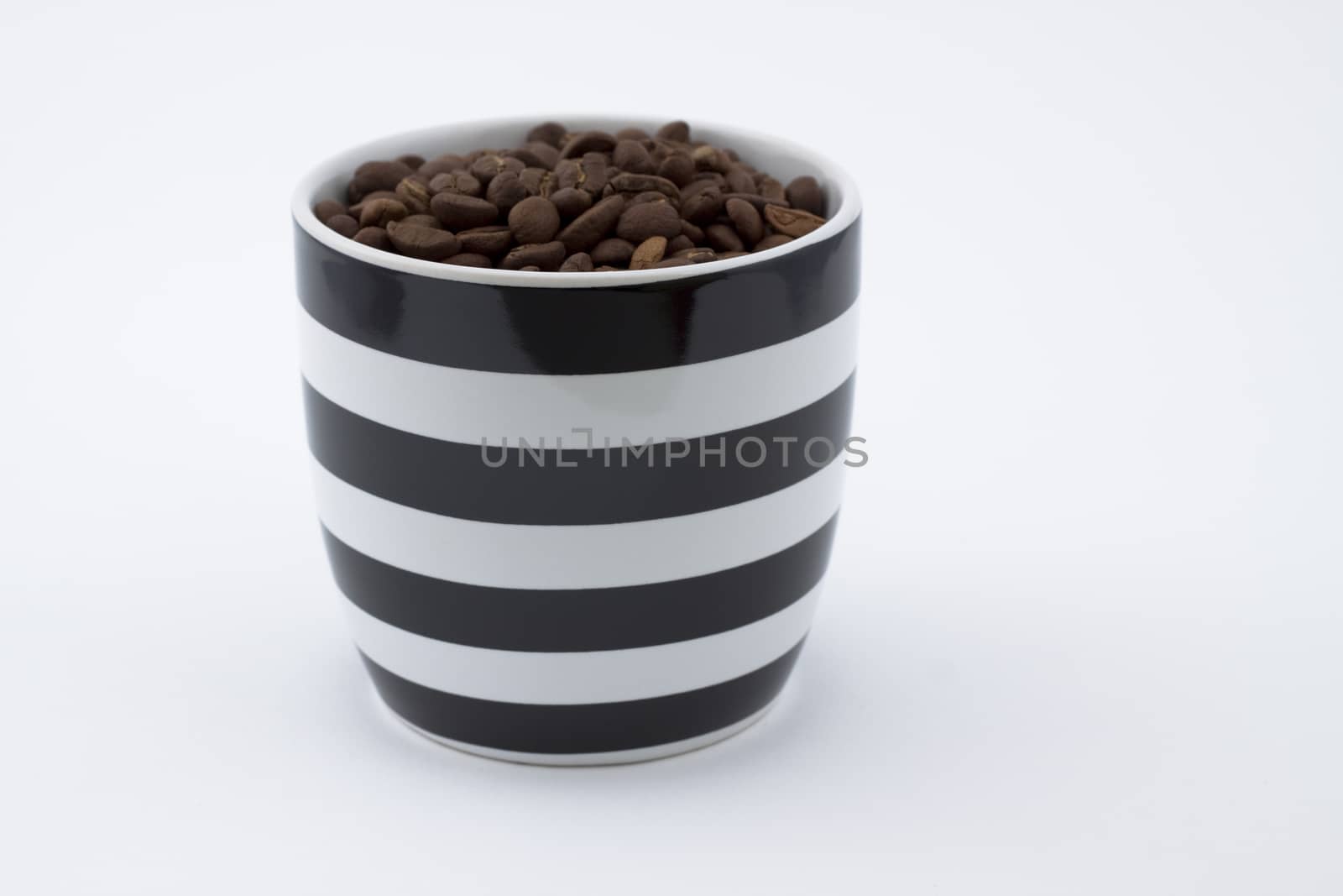 white and black mug full of brown coffee beans on white background