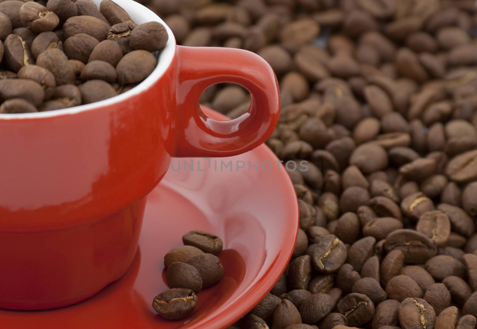 red coffee cup full of coffee beans  and coffee beans all around closeup