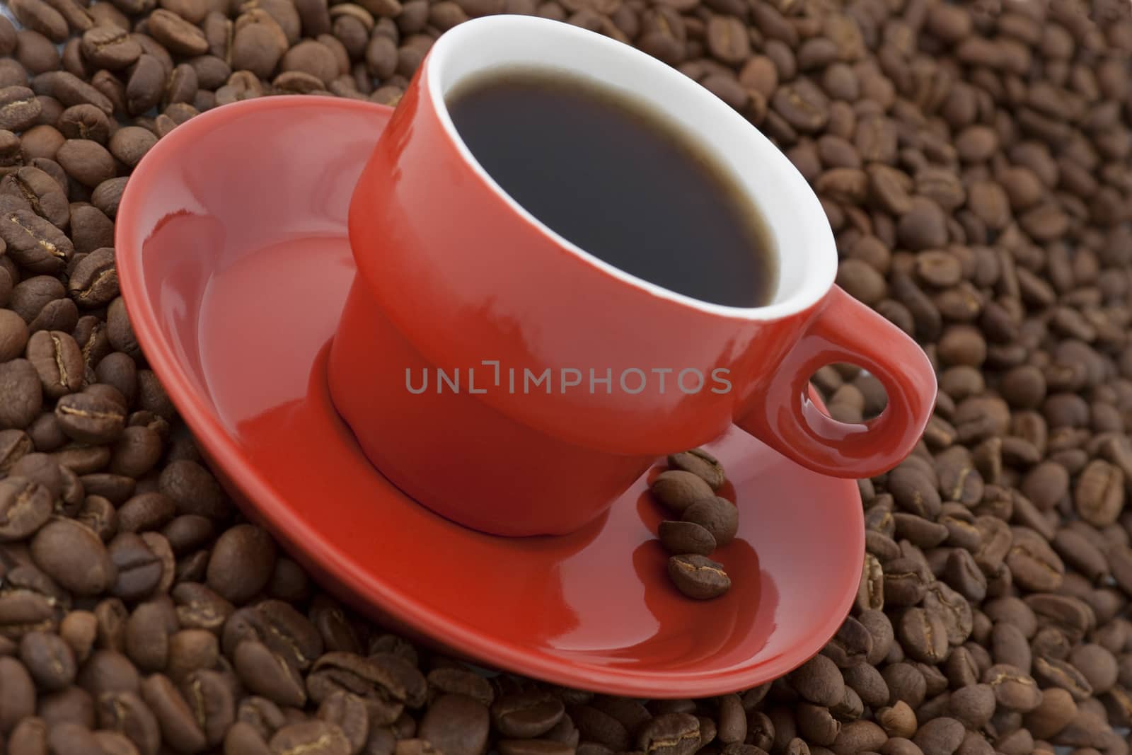 diagonal view of red coffee cup with plate full of coffee beans on white background