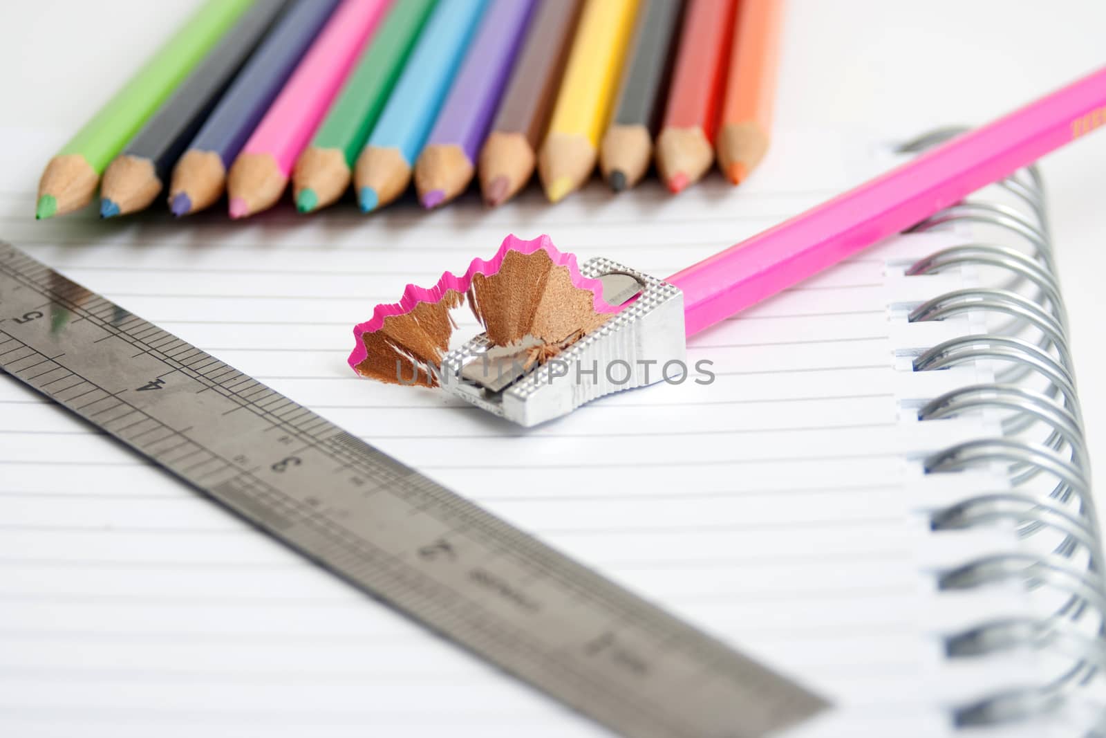 colored pencils on a note pad with a ruler on white background