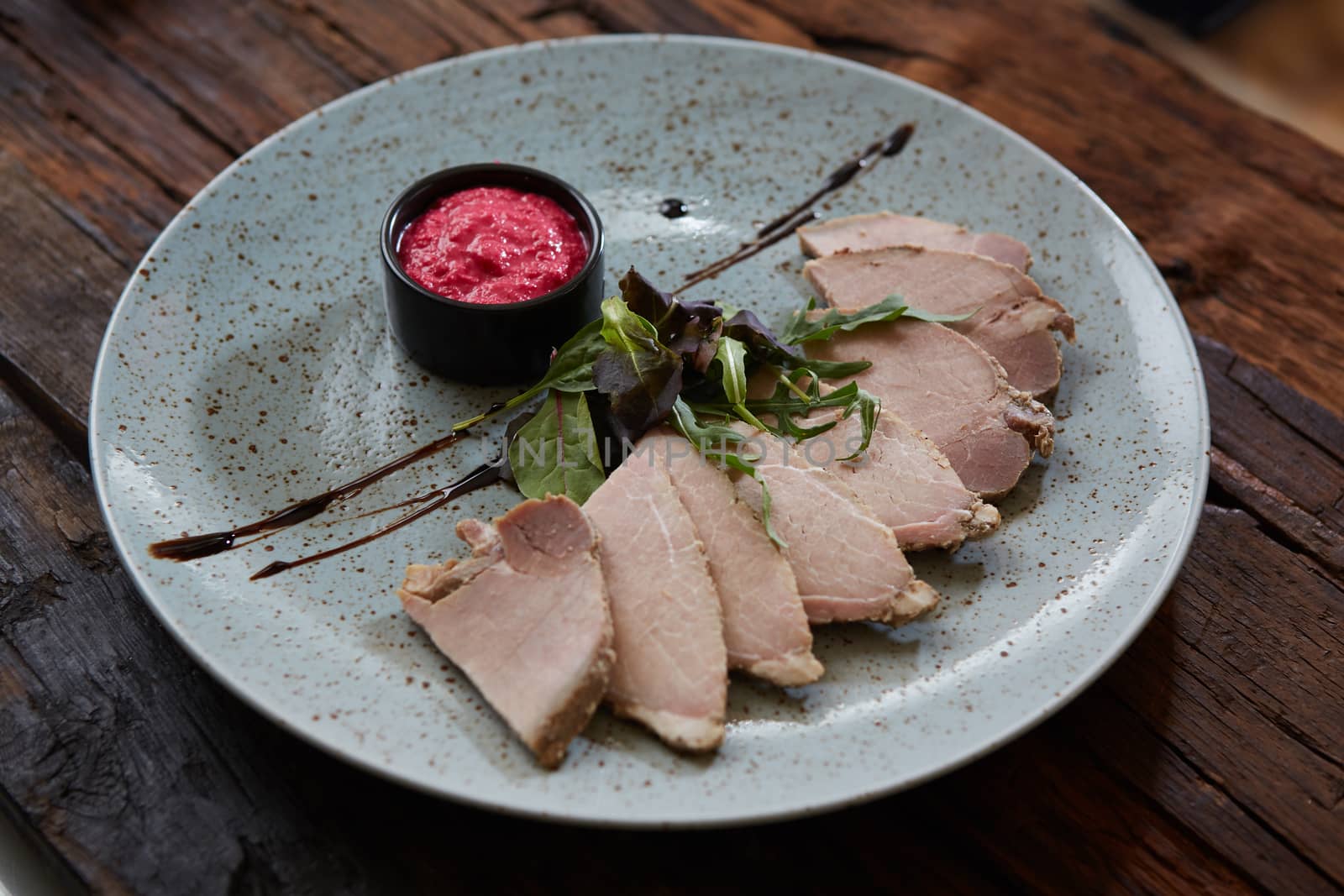 Sliced cold baked pork with herbs on blue plate.