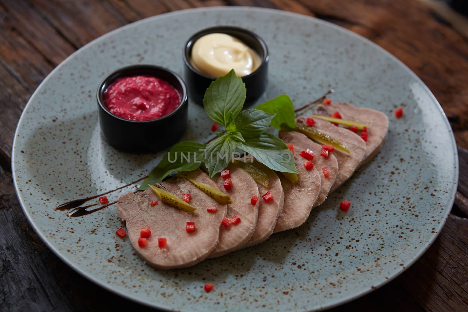 Sliced cold baked pork with herbs on blue plate.