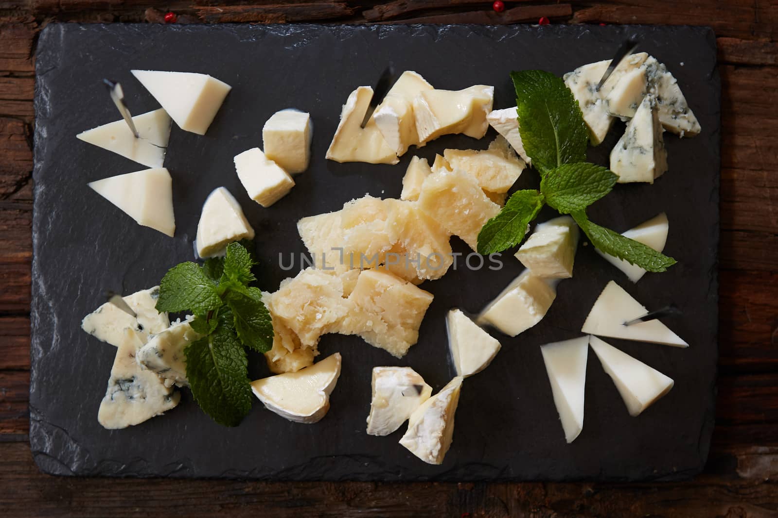 Cheeseboard with Sliced Limburger, Herve Cheese or Reblochon And Blue Gorgonzola, Roquefort or Stilton. Cheese Course with Mix of Yellow and Blue Cheeses Top View on Black Stone Plate Background