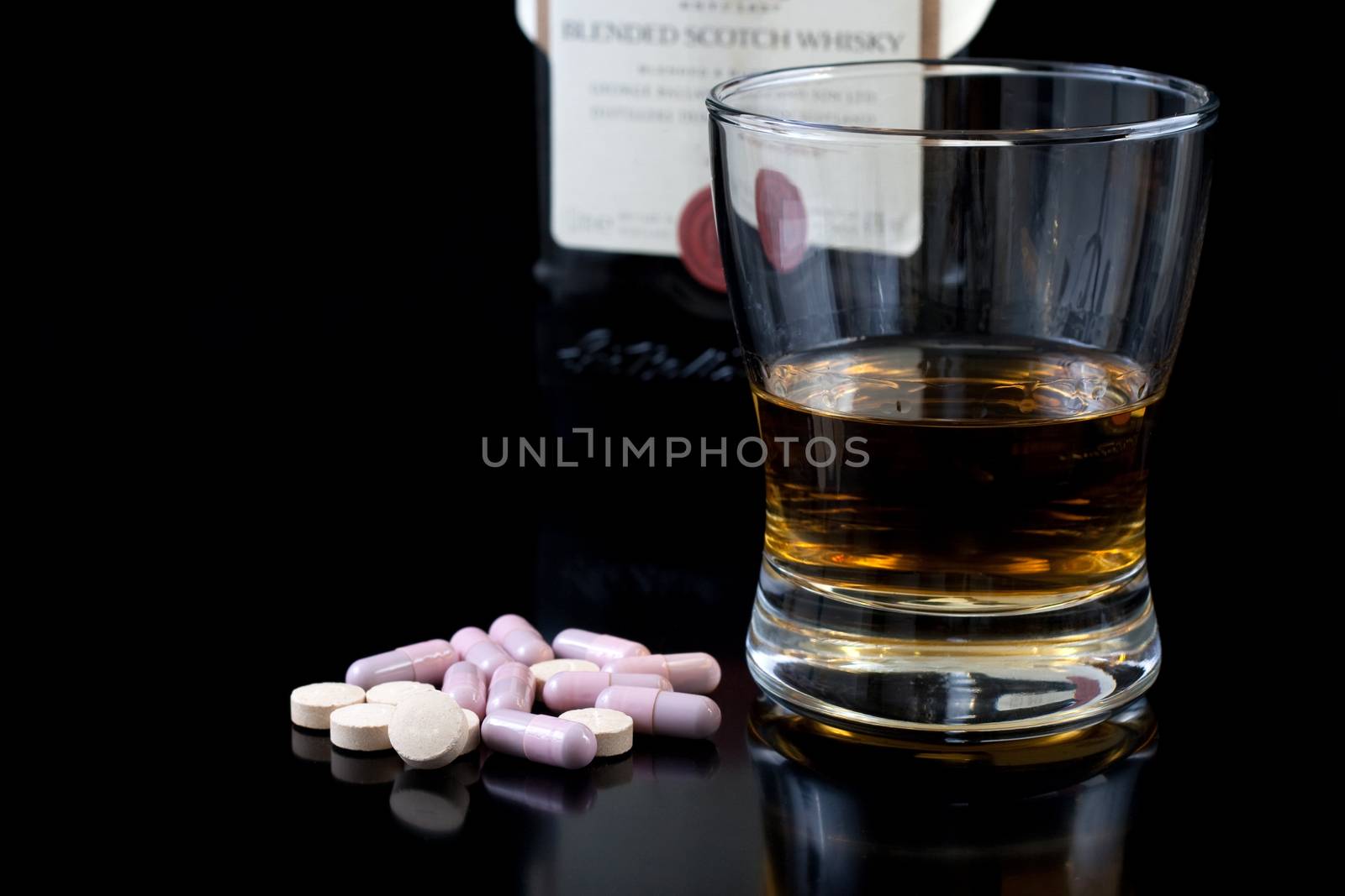 wiskey in a glass some pills and the bottle behind on black background