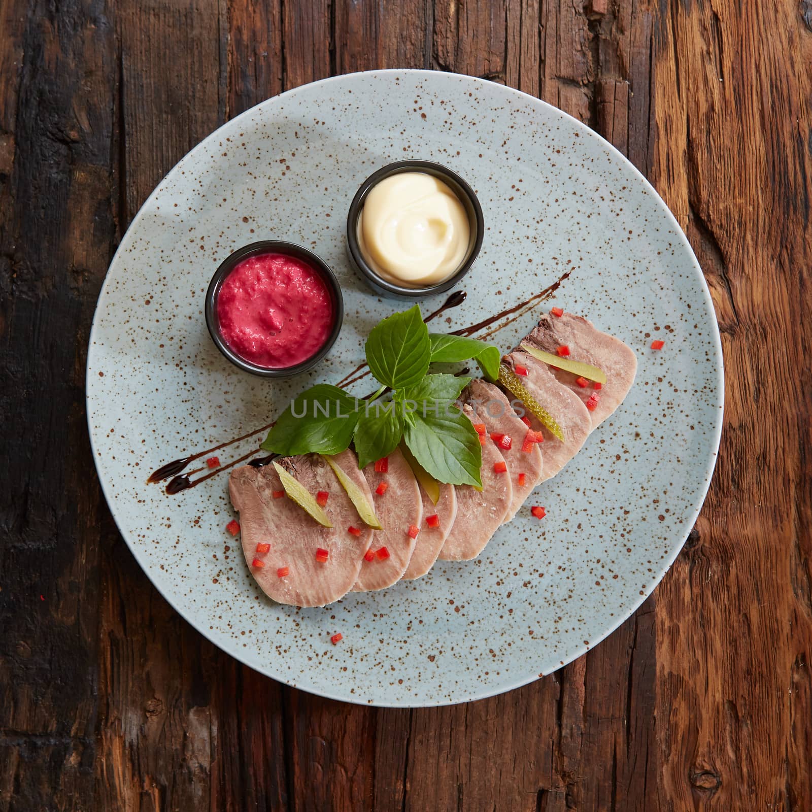 Sliced cold baked pork with herbs on blue plate.