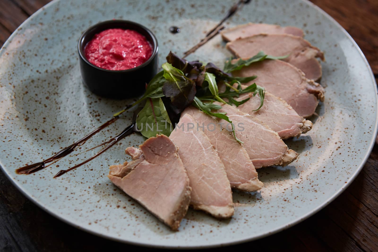 Sliced cold baked pork with herbs on blue plate.